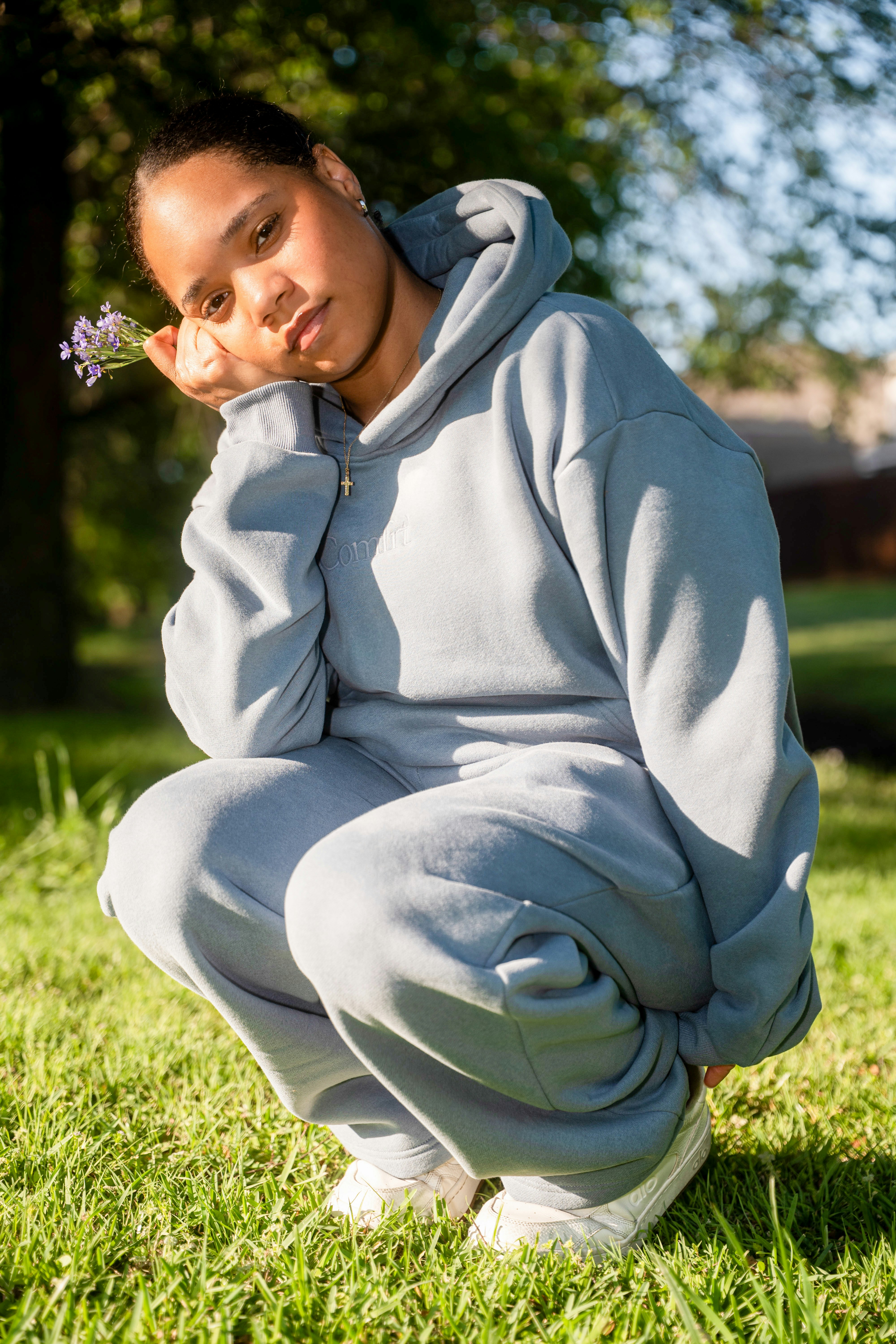 A young woman in a blue tracksuit squats in grass.