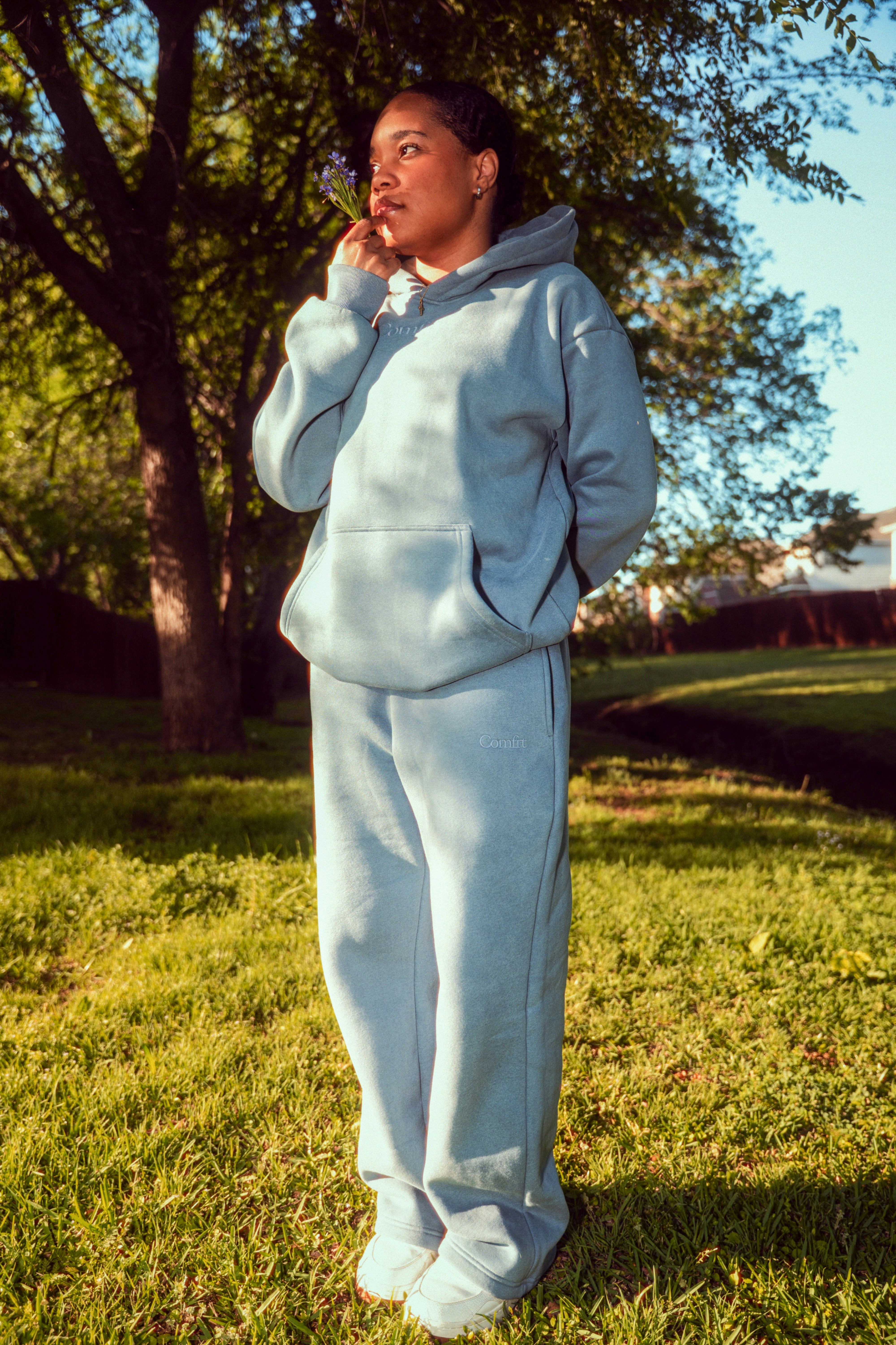 A young woman in a blue tracksuit smelling a flower.