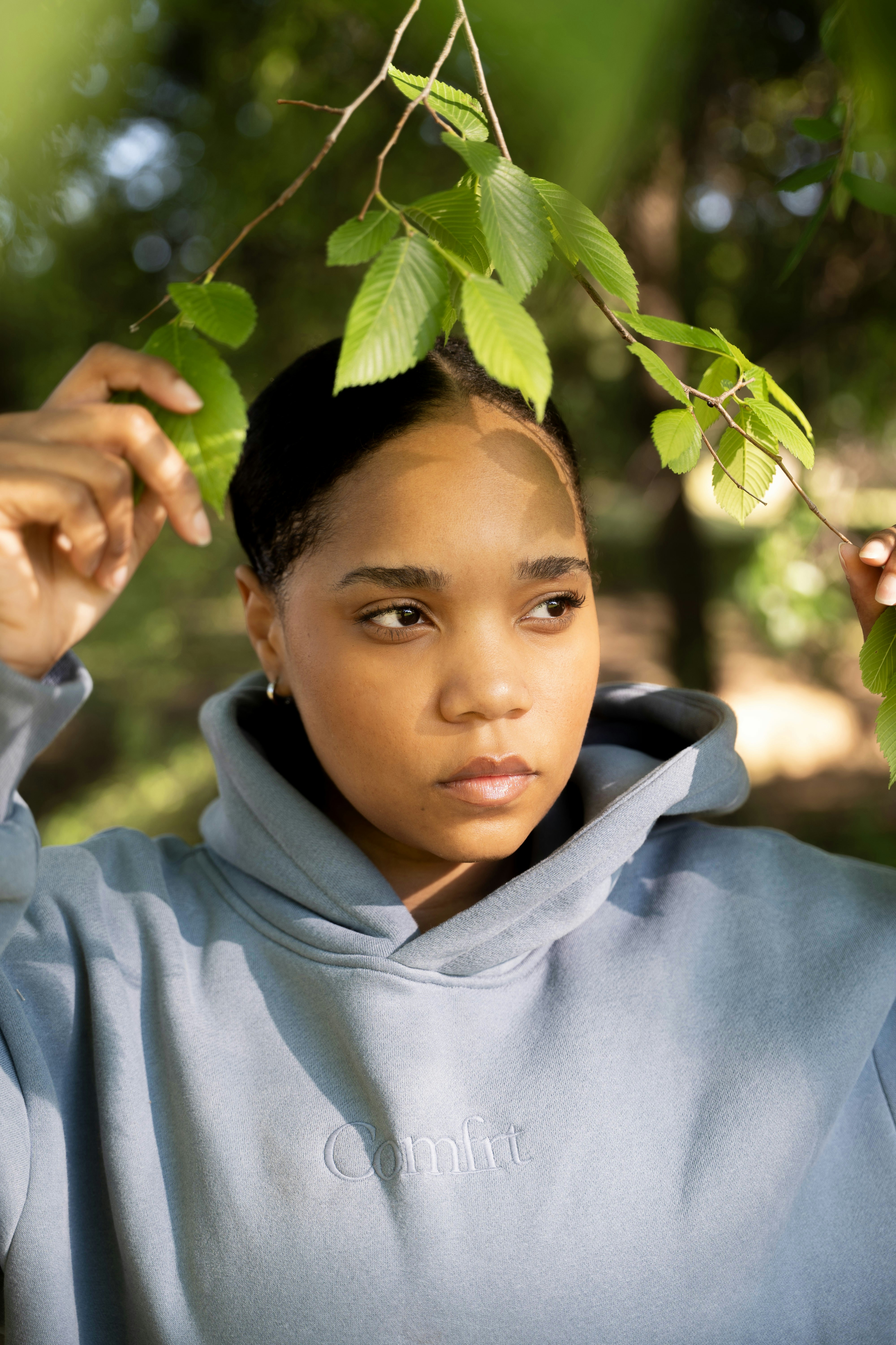 Young woman in a hoodie holding branches with leaves