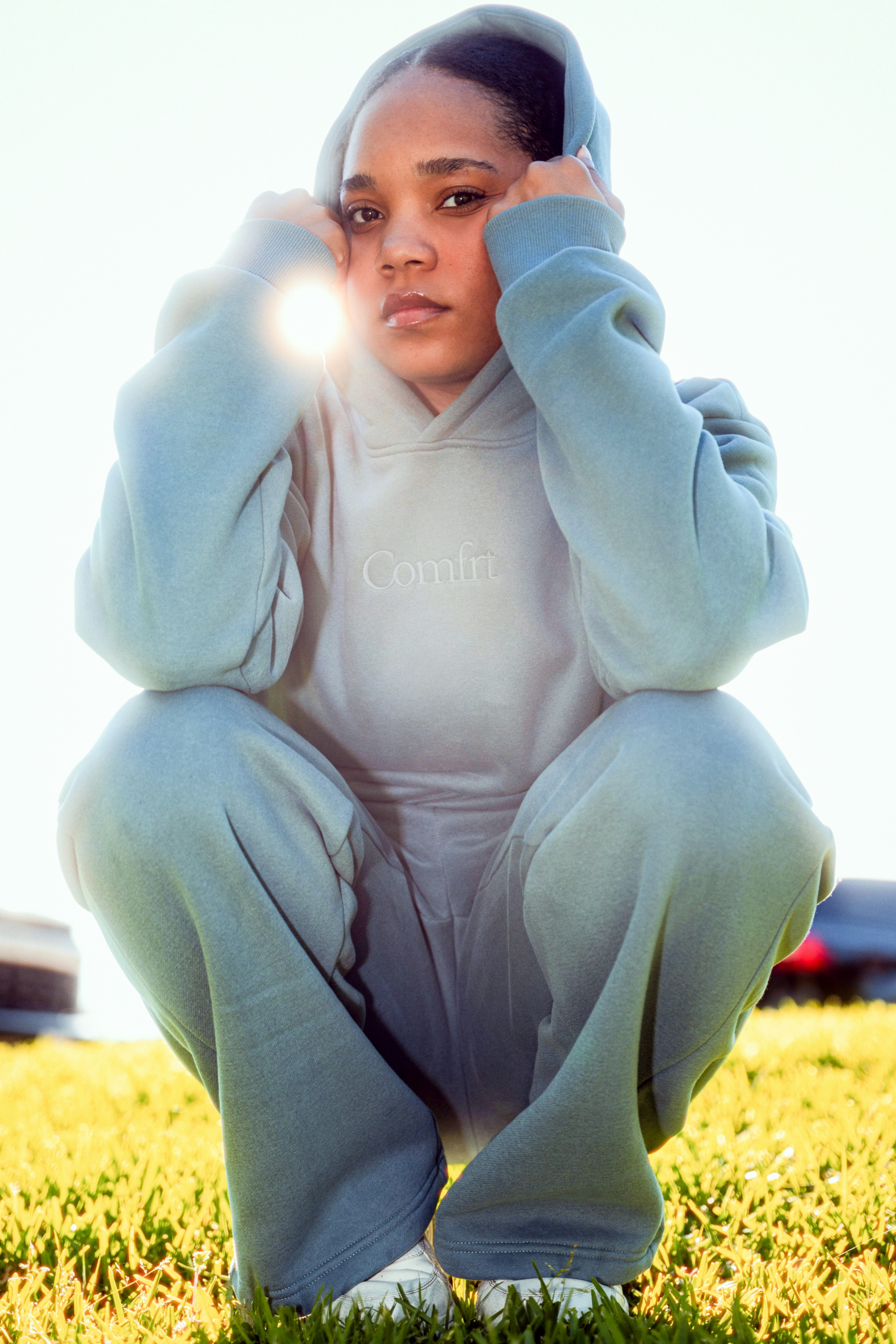 A young woman in a blue tracksuit squats outdoors.