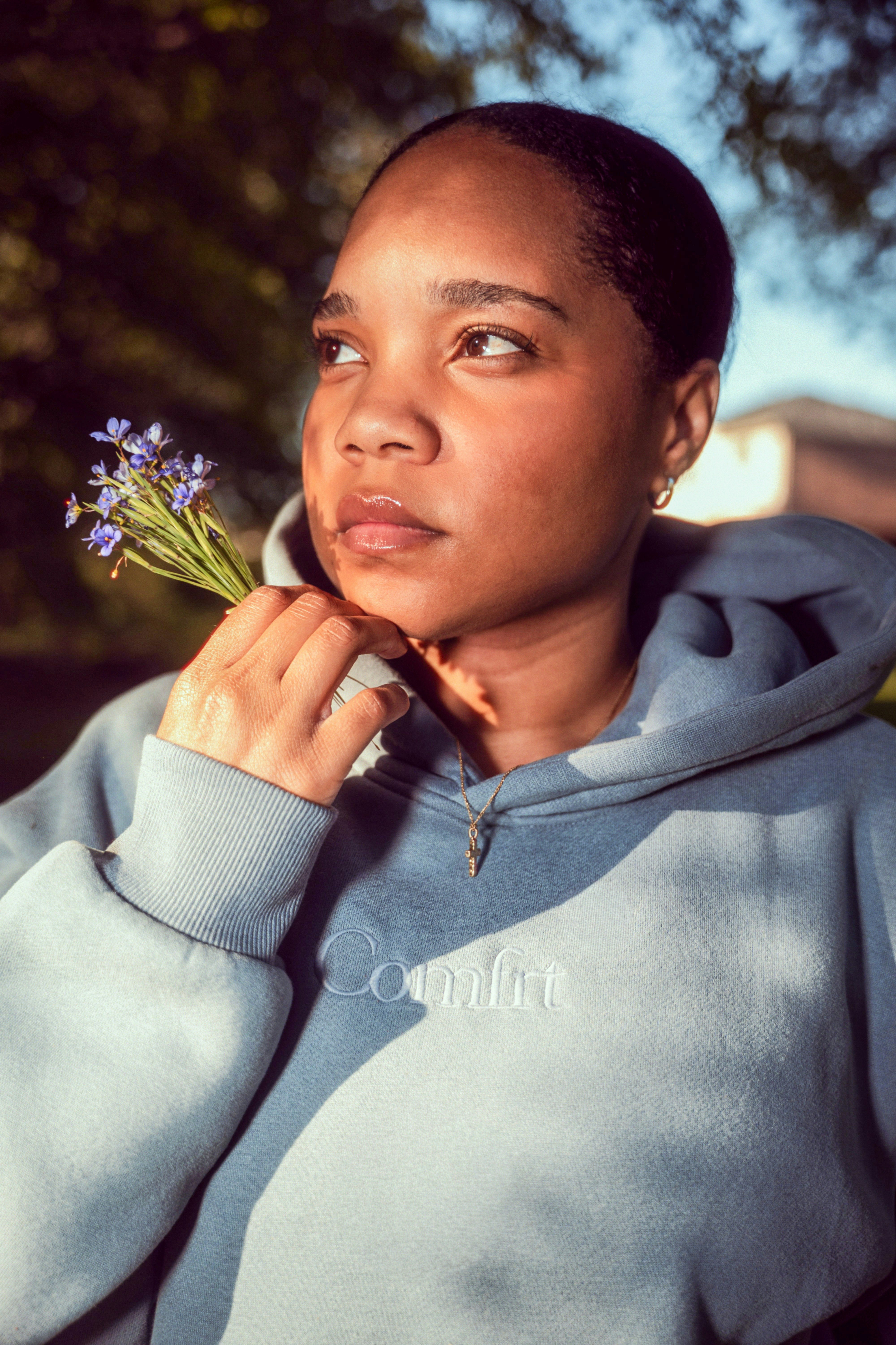 Young woman holding a small bouquet of purple flowers.