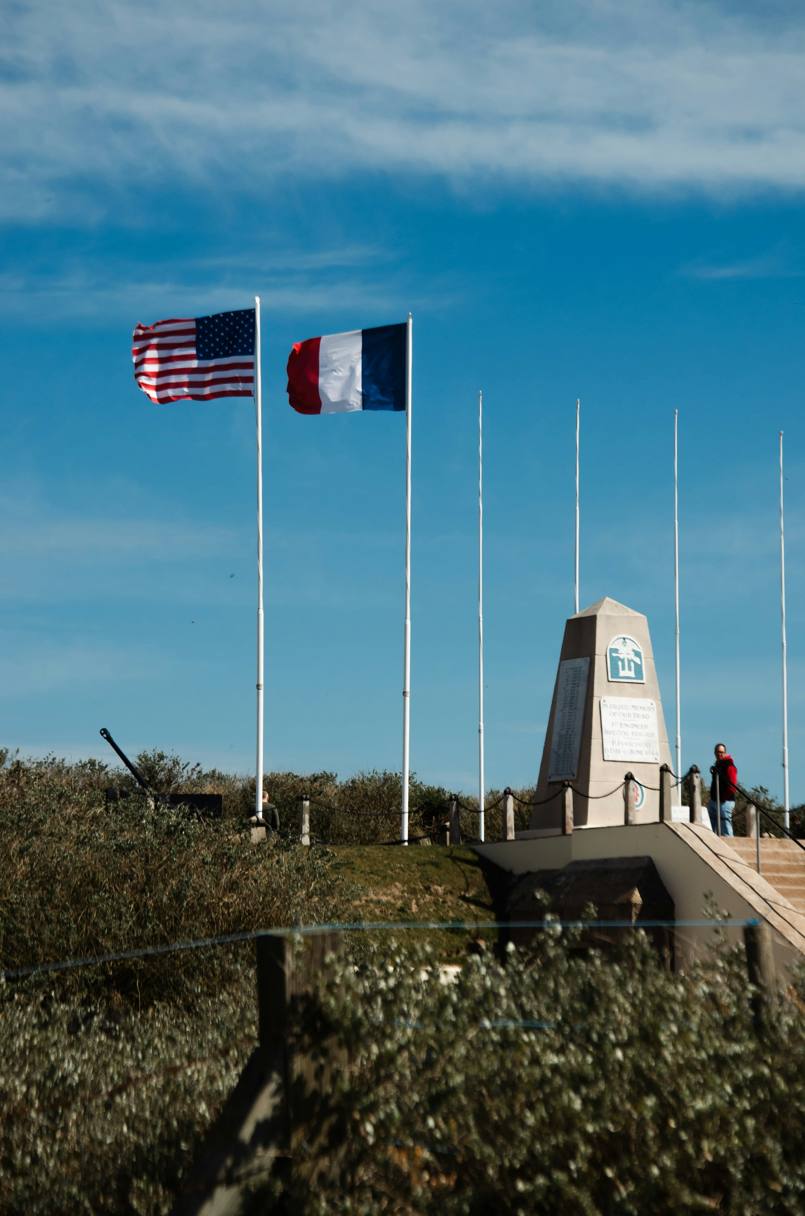 American and french flags fly near a monument.