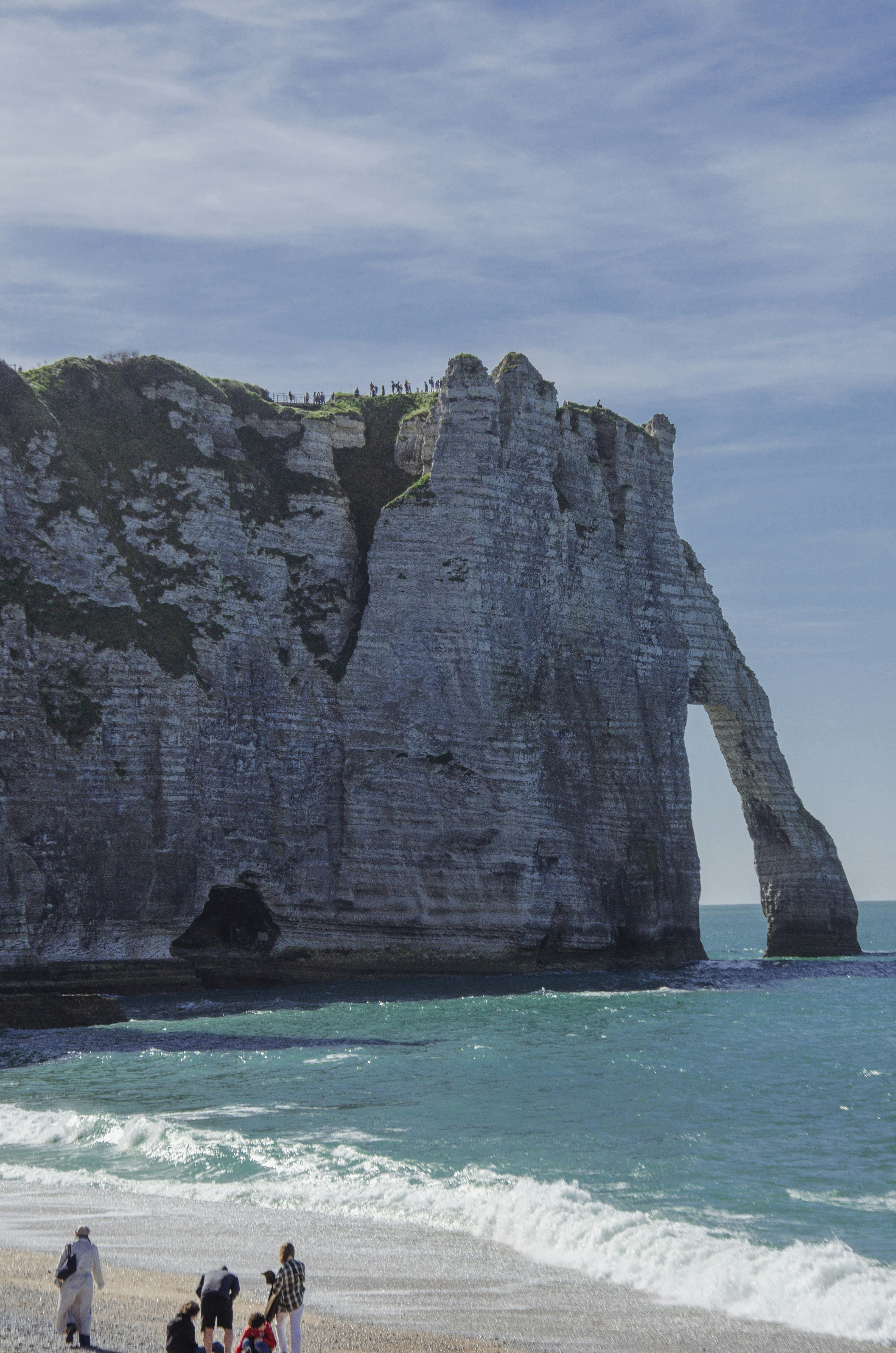 People on a beach with a large rock arch formation.