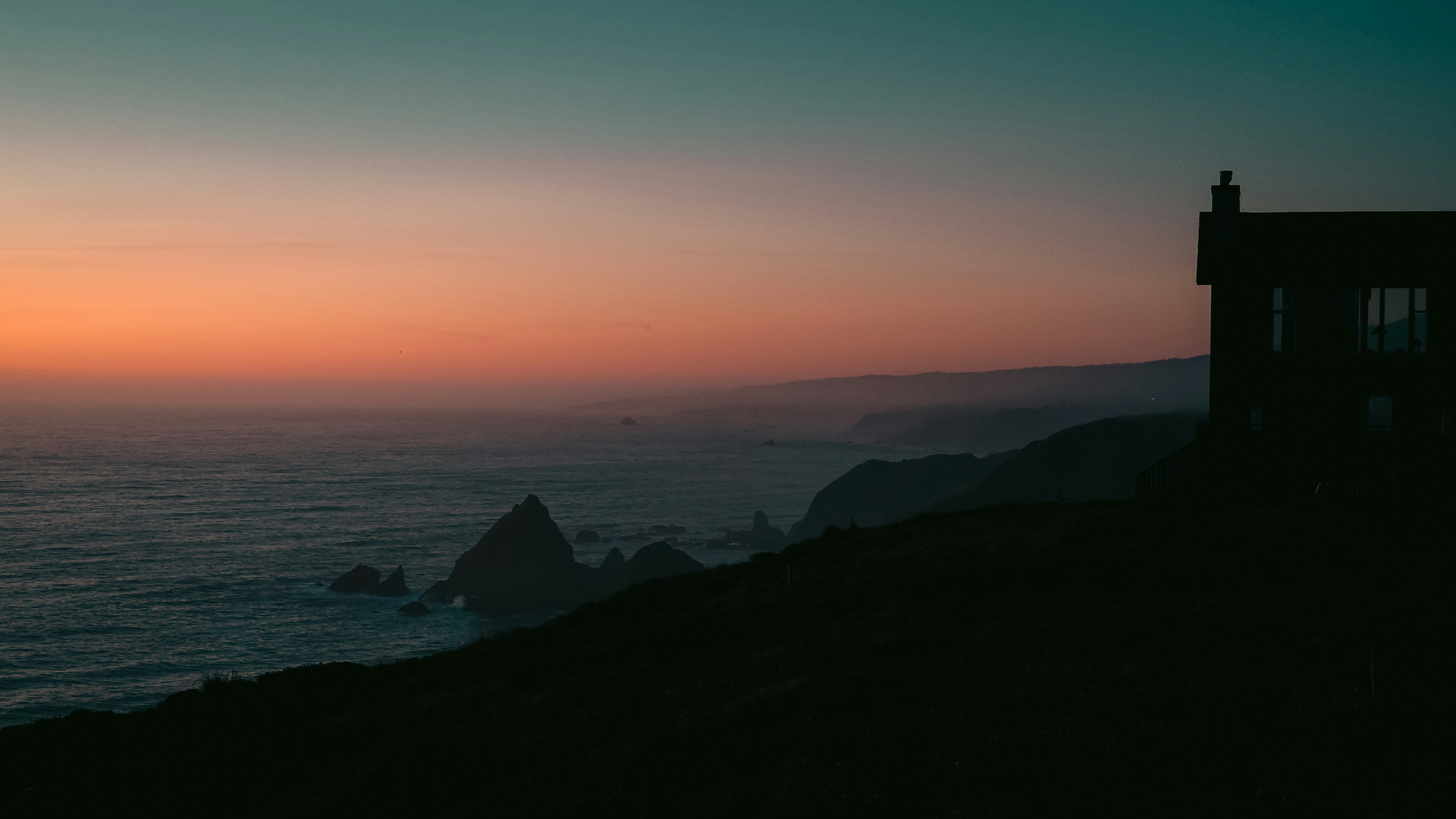 Silhouette of a house overlooking the ocean at sunset