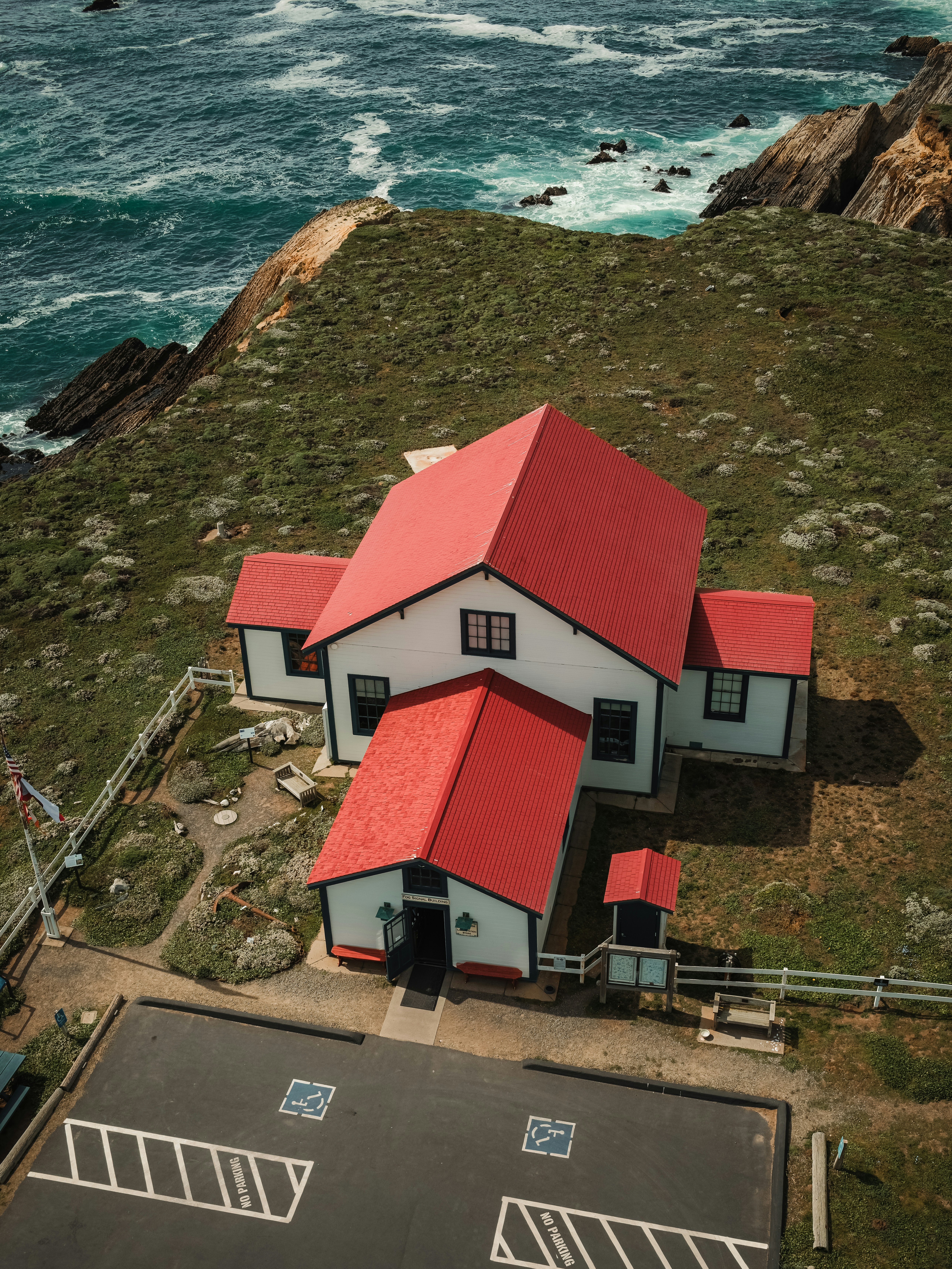 White house with red roof on grassy cliff by ocean