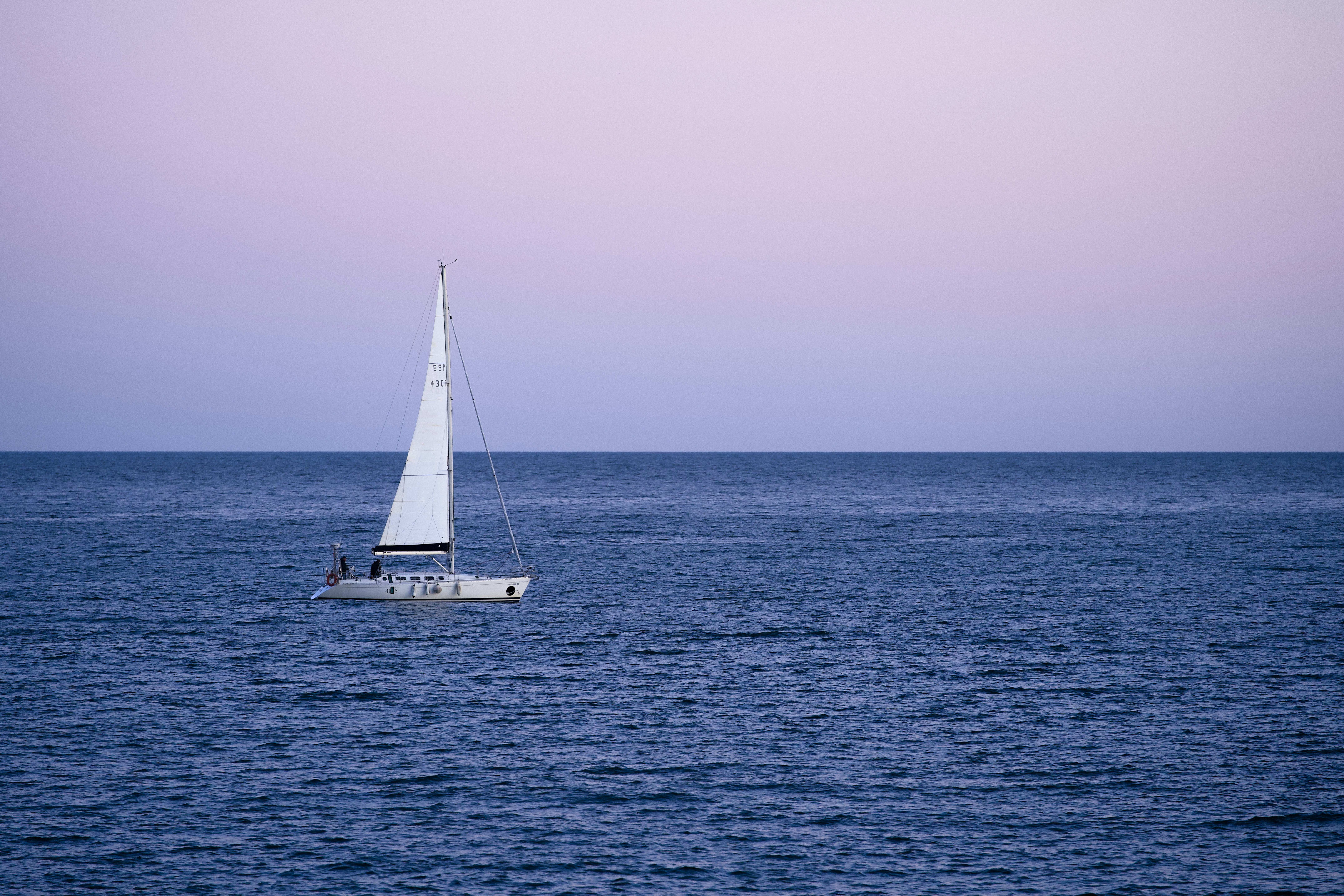 Un velero solitario se desliza sobre un océano azul y tranquilo.