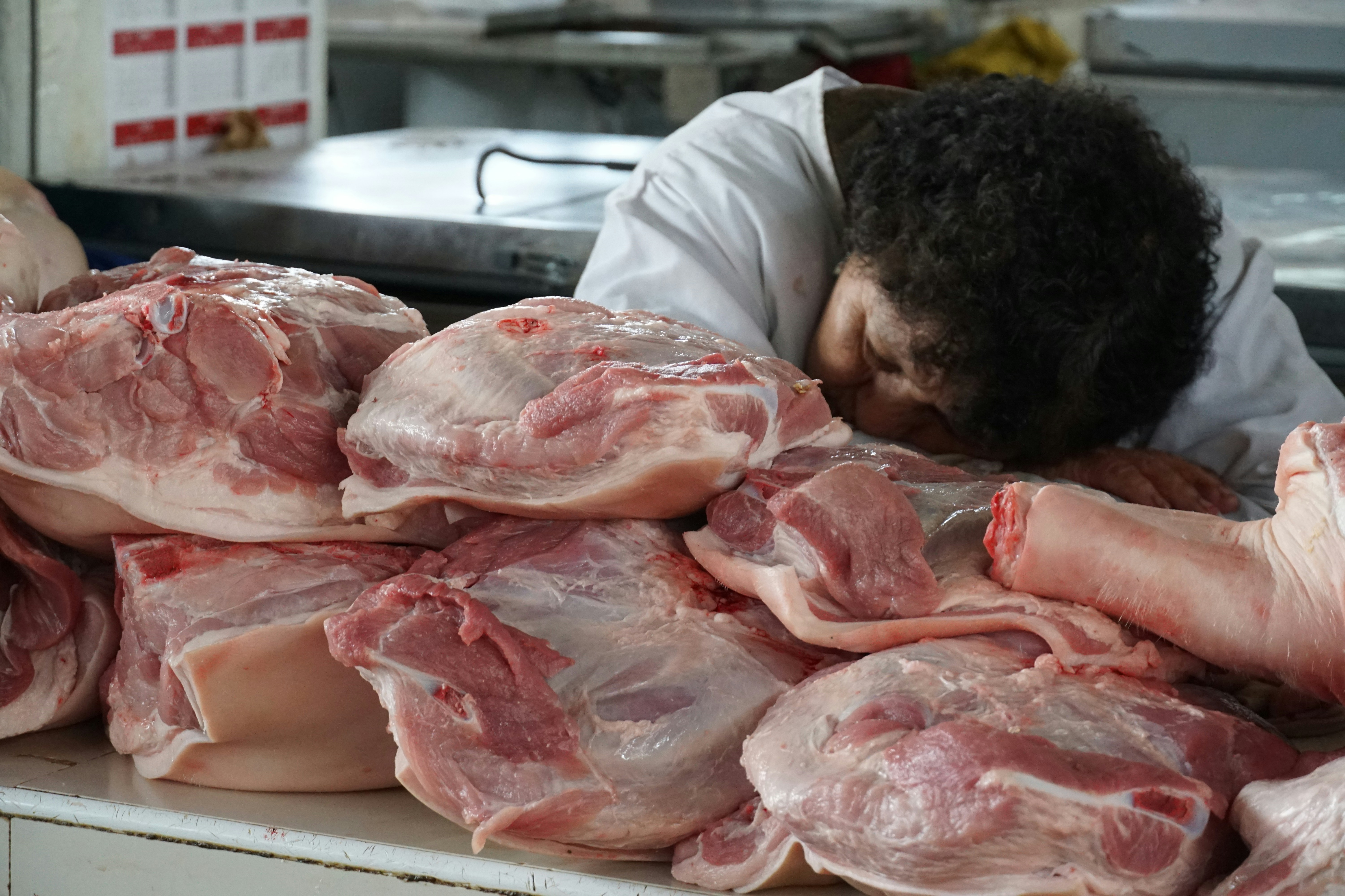 Butcher rests head on pile of raw pork cuts