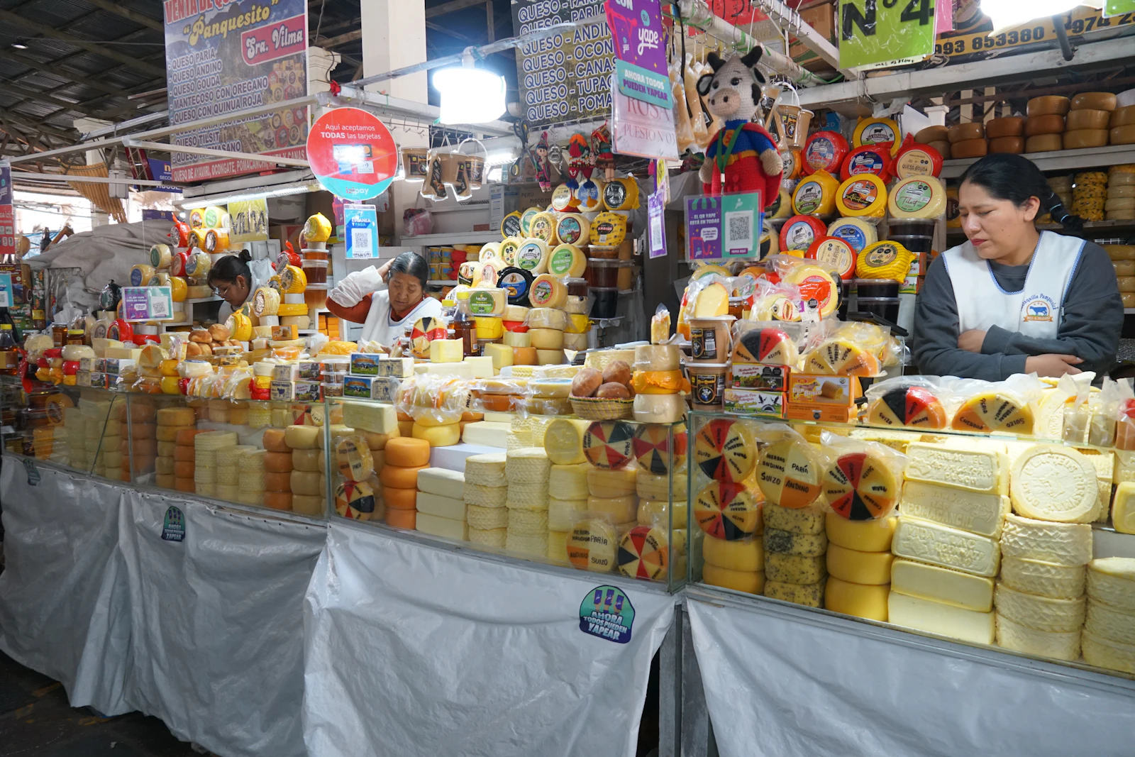 A market stall piled high with wheels of Andean cheese at a covered market in Cusco, the vendor arranging her display