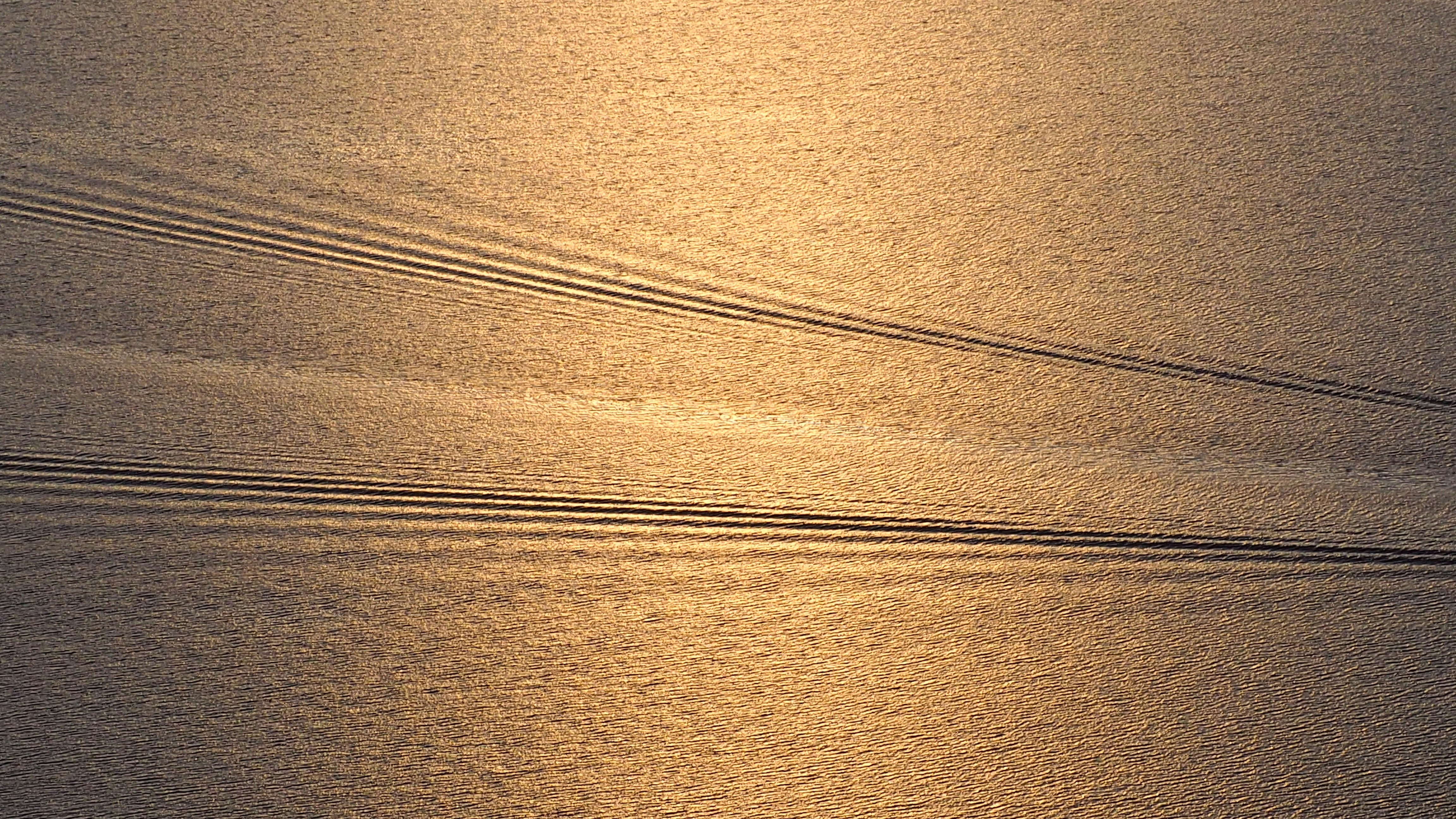 Boat wakes create lines on golden water surface