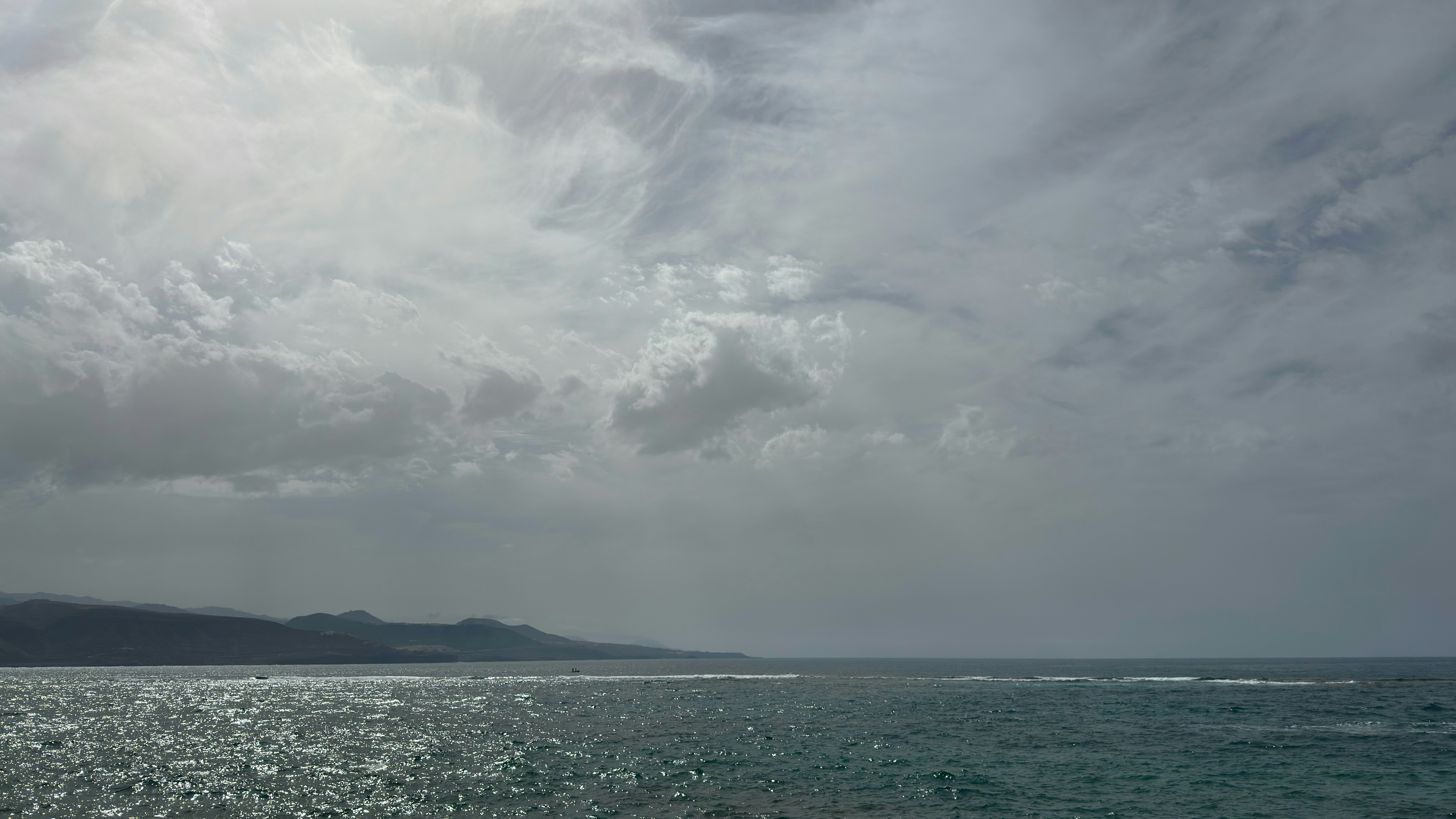 Ocean waves under a cloudy sky with distant coastline