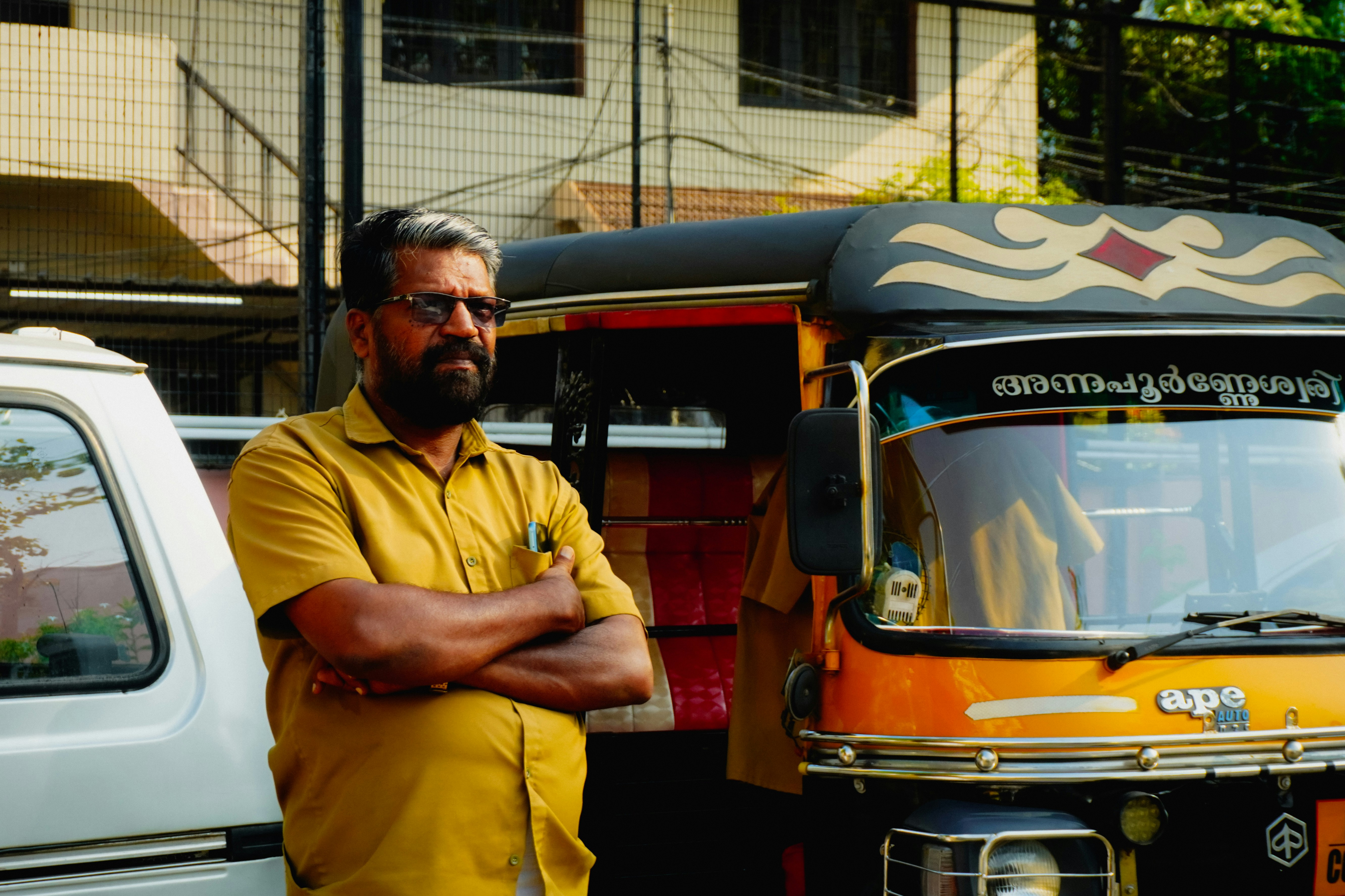 Hombre con camisa amarilla de pie junto a un auto-rickshaw