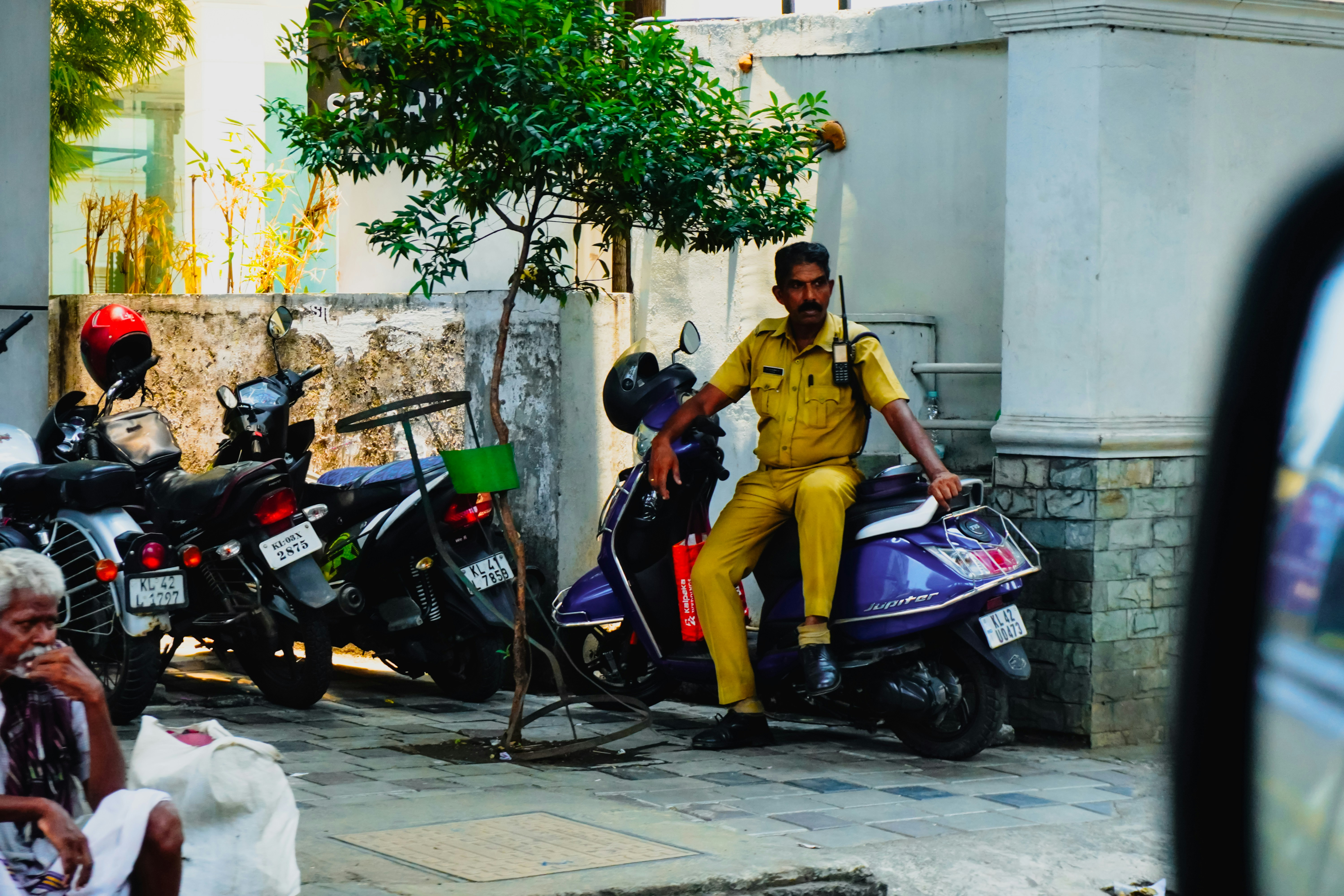 Man in yellow uniform sits on a scooter.