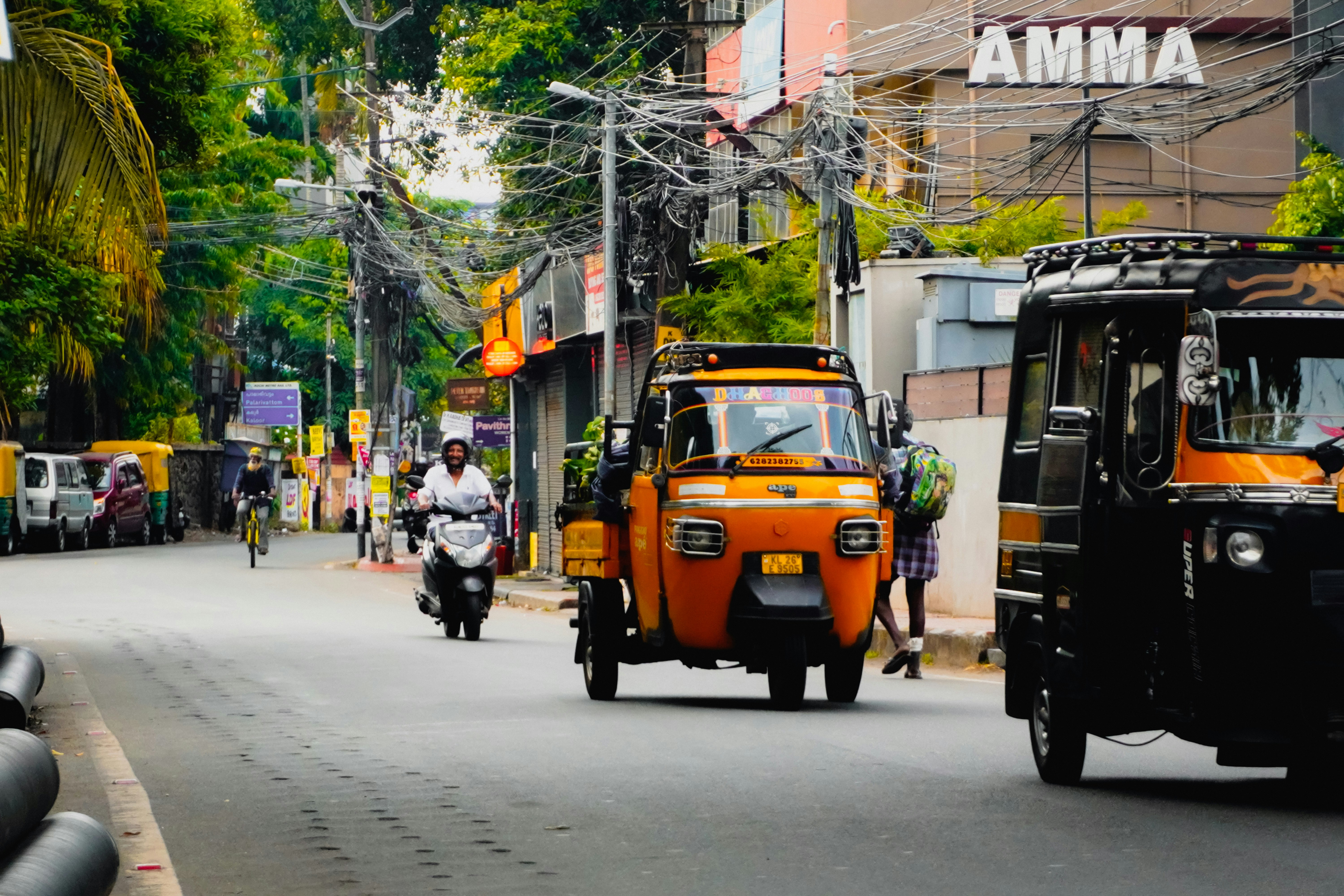 Orange auto-rickshaw drives down a busy street.