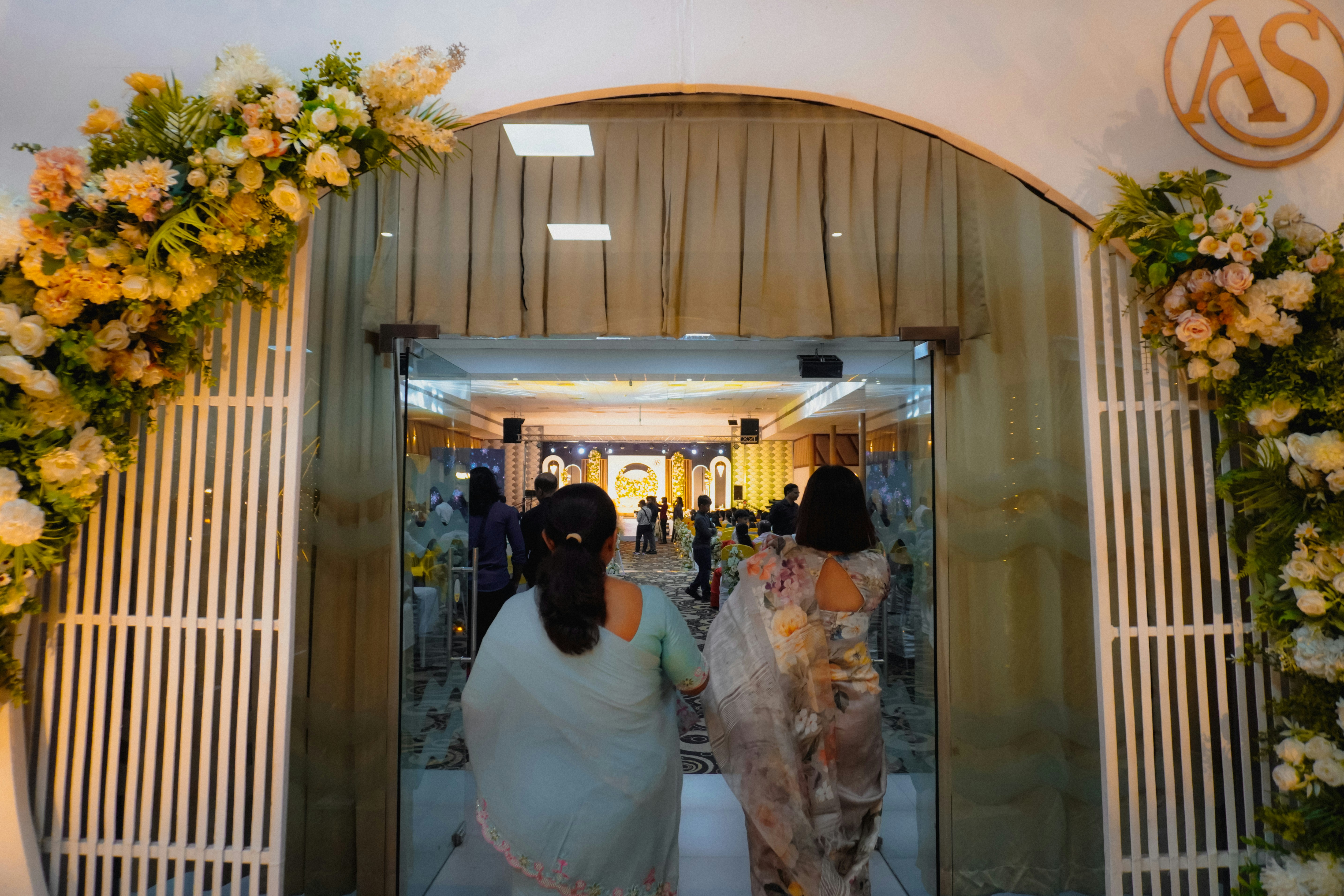Gente entrando en un salón decorado con arreglos florales.