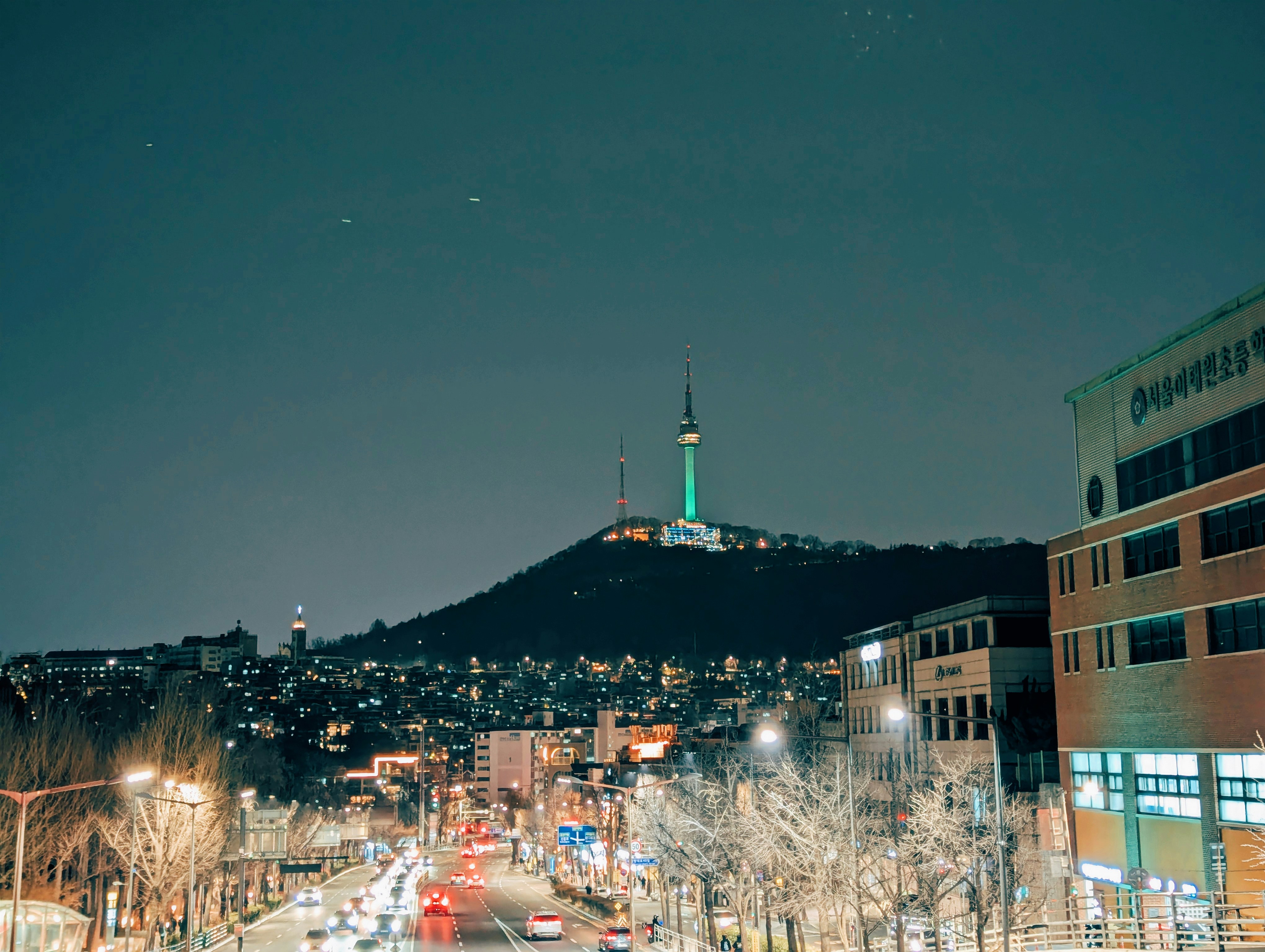 Cityscape at night with a prominent tower on a hill.