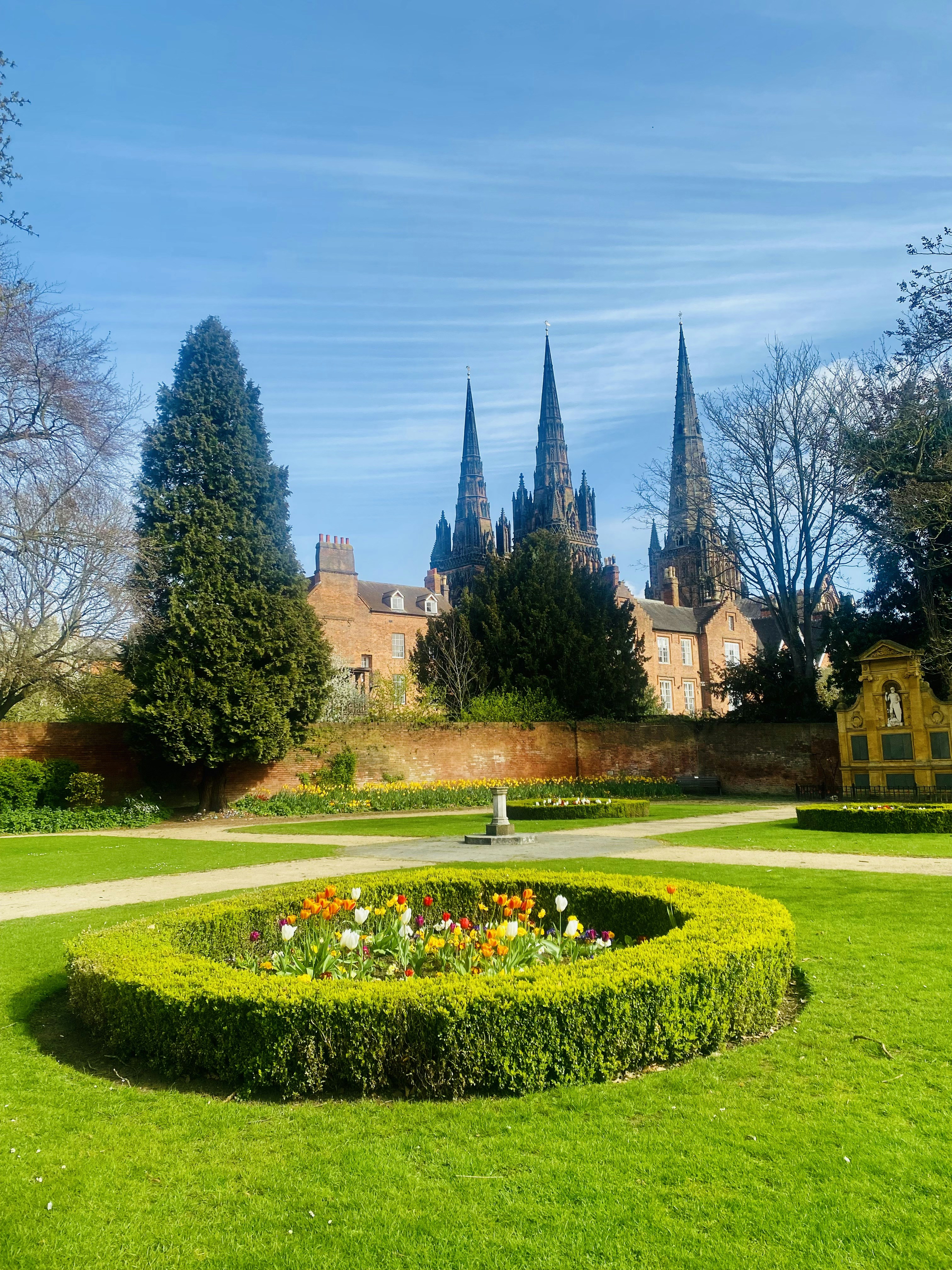 Un parc ensoleillé avec un parterre de fleurs circulaire et une cathédrale.