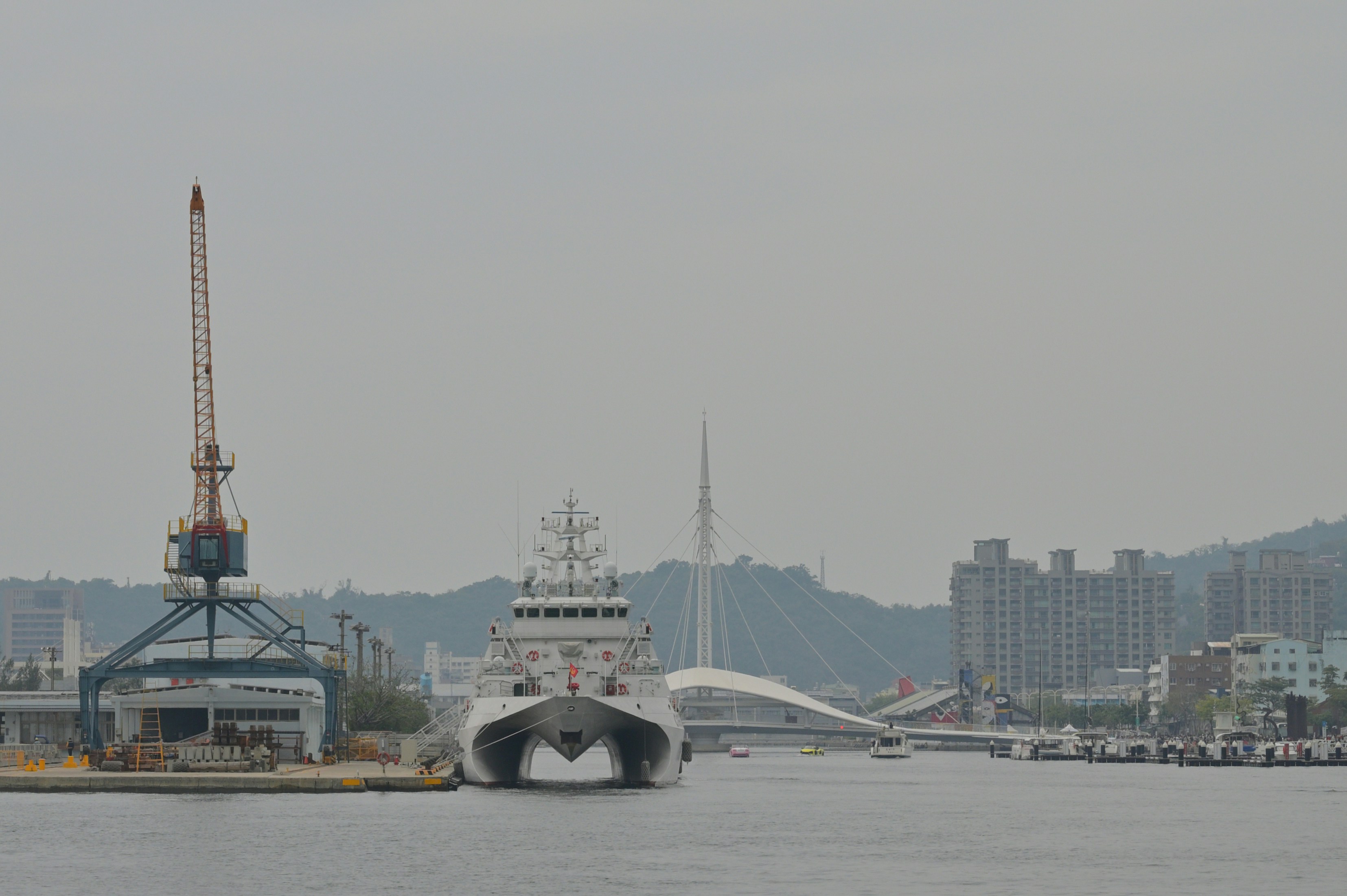 Modern catamaran yacht docked at a harbor with cranes