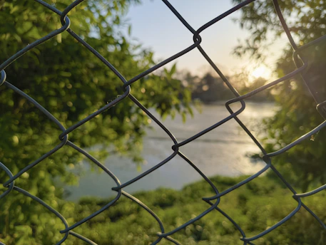 Sunset over a calm lake seen through a fence.