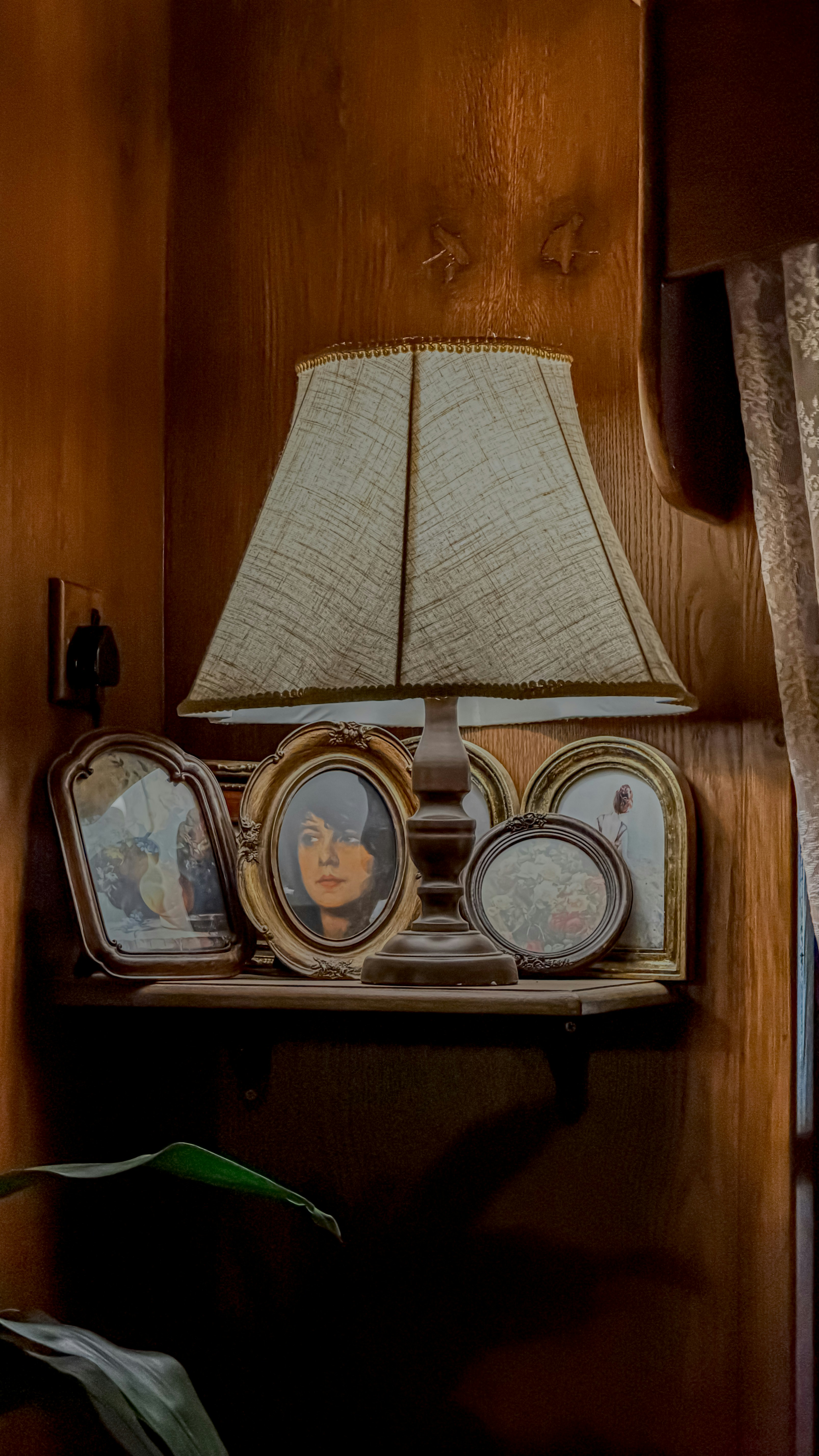 Une lampe et des portraits encadrés sur une étagère en bois.