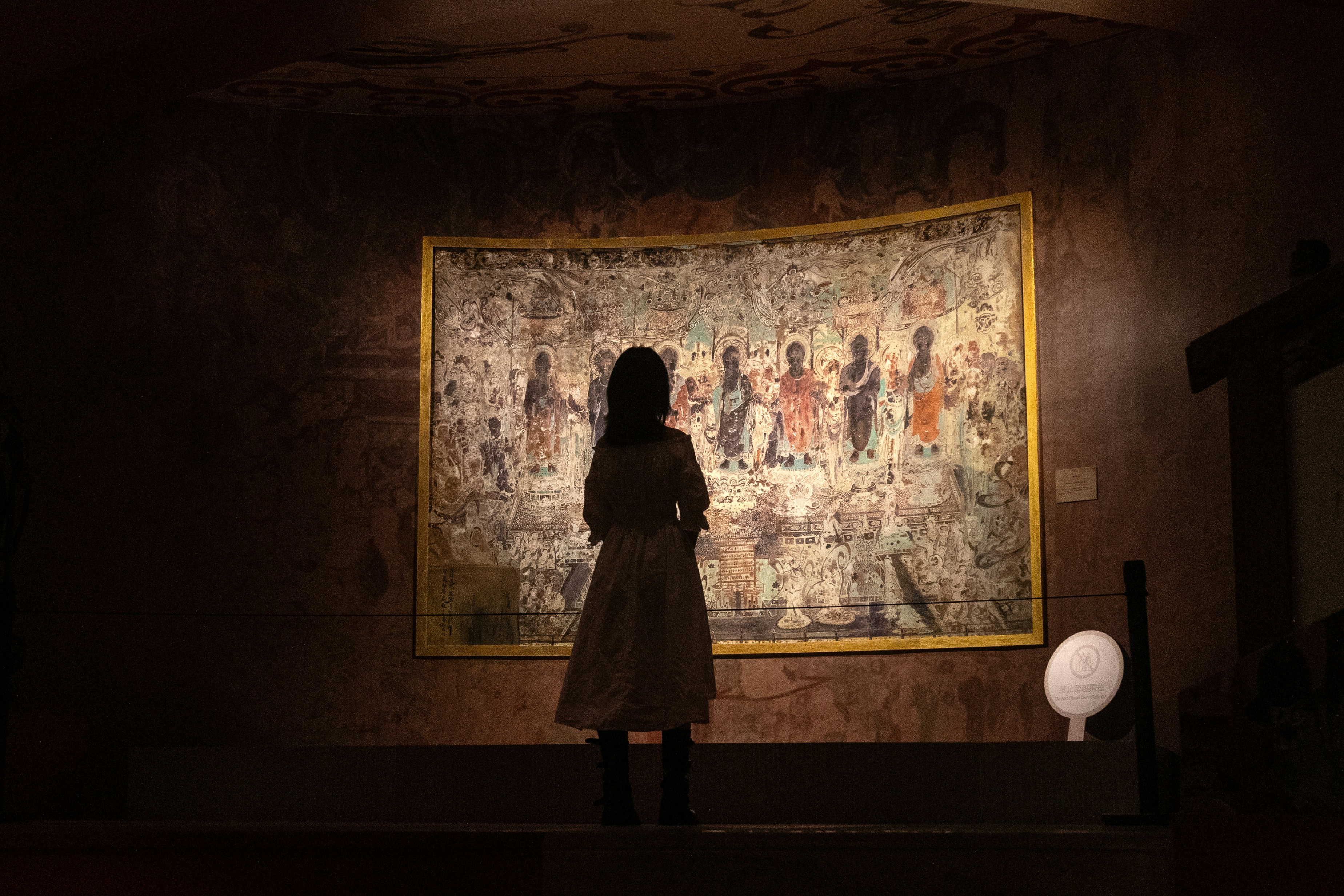 Femme regardant des œuvres d’art anciennes dans un musée faiblement éclairé.