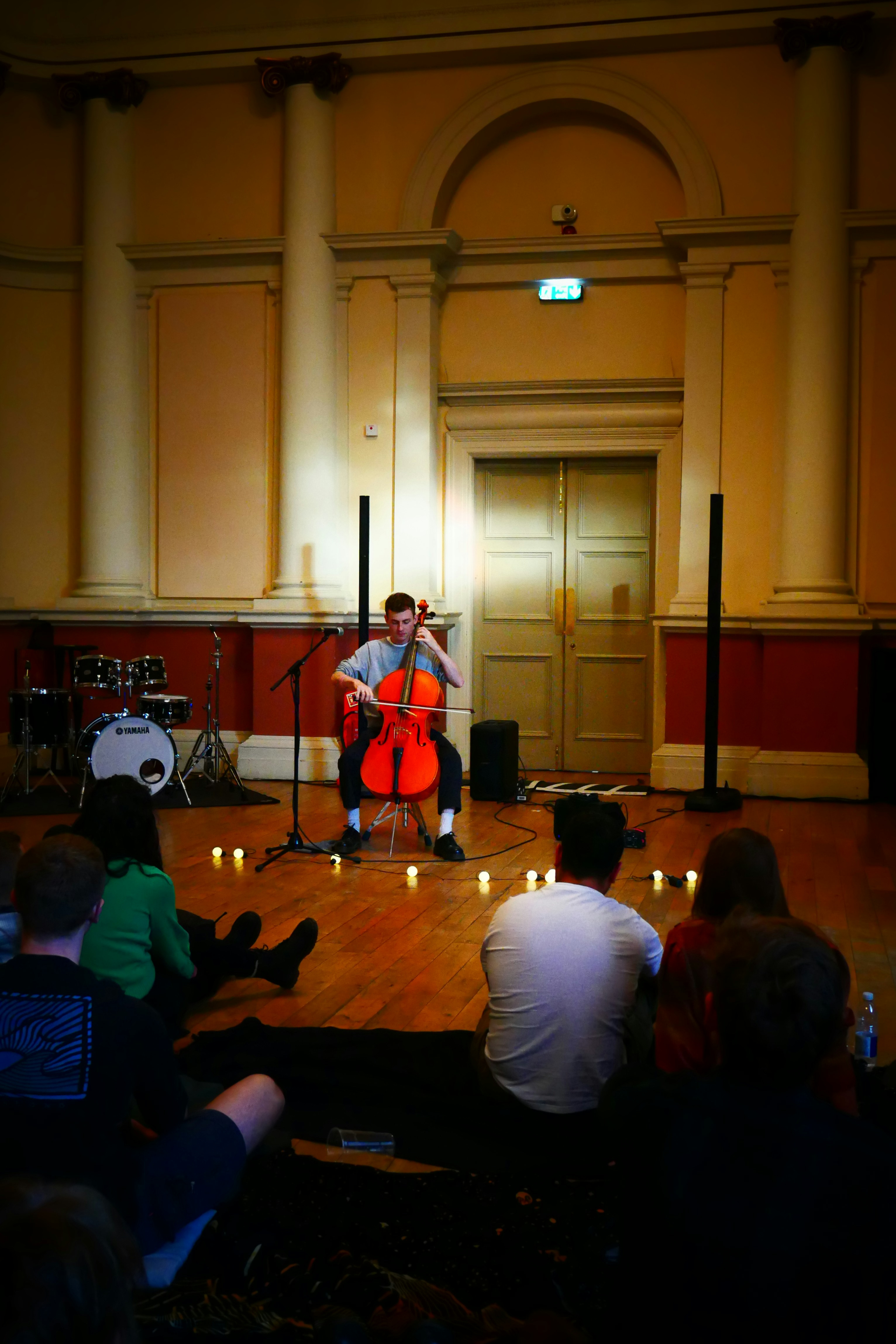 Uomo suona il violoncello circondato da candele per un pubblico