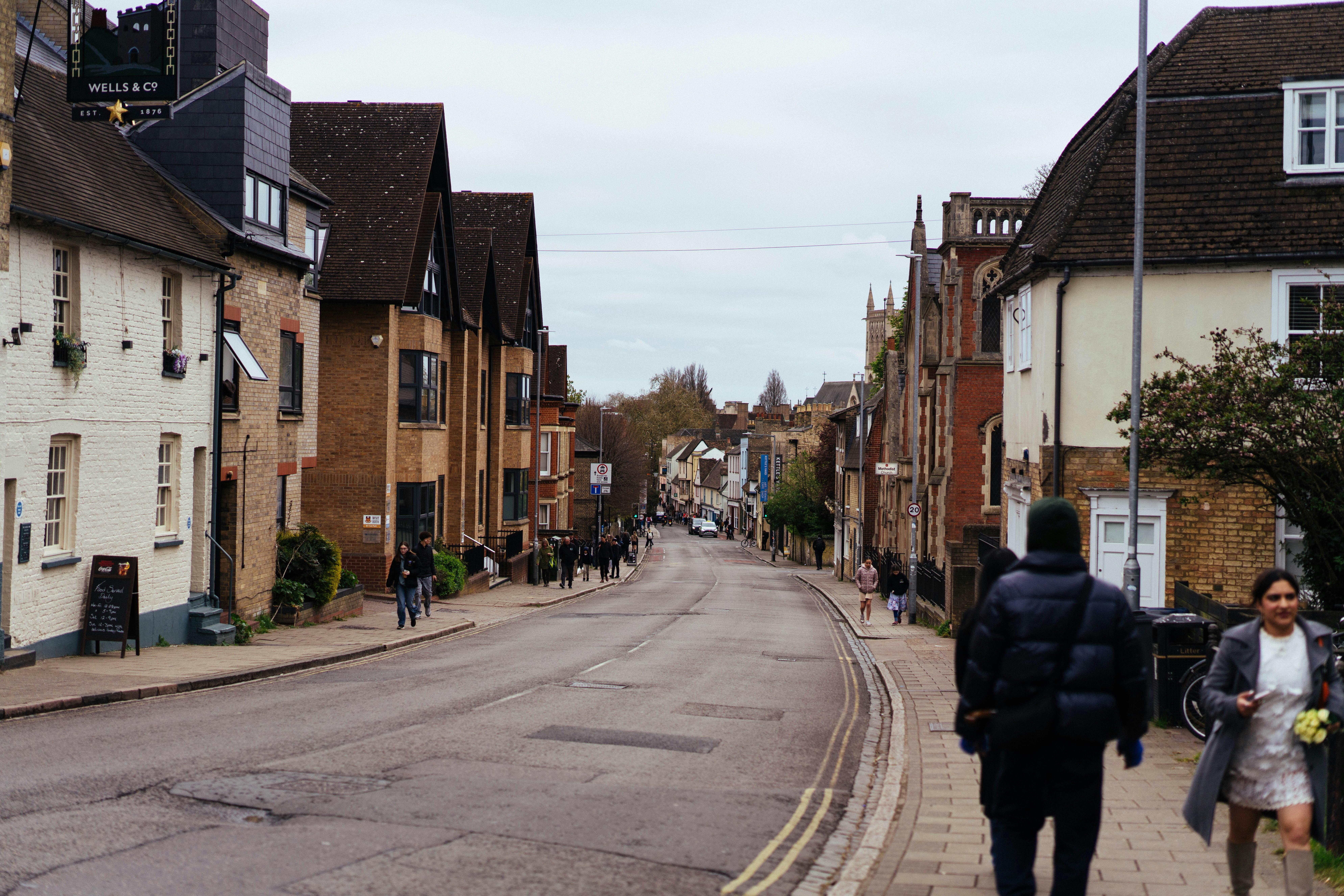 人々は古い建物のある木々に囲まれた通りを歩いています。