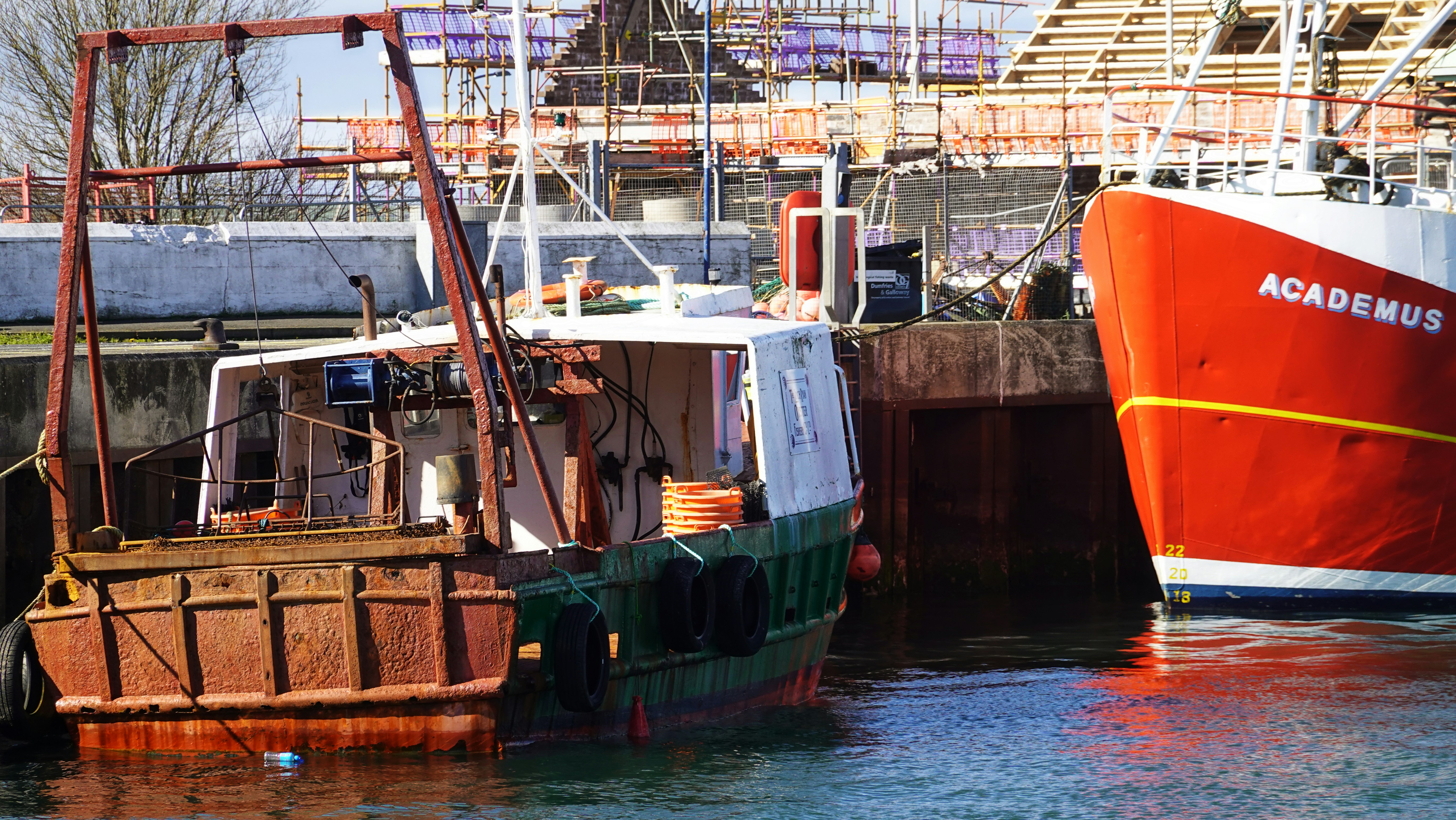 Two boats docked at a harbor with construction in background