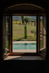Open window view of a swimming pool and tuscan landscape.