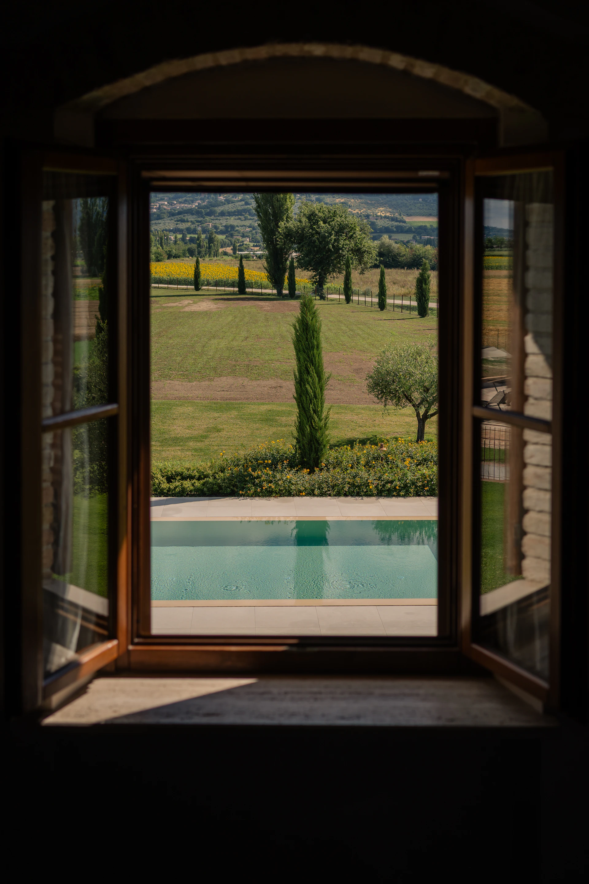 Open window view of a swimming pool and tuscan landscape.