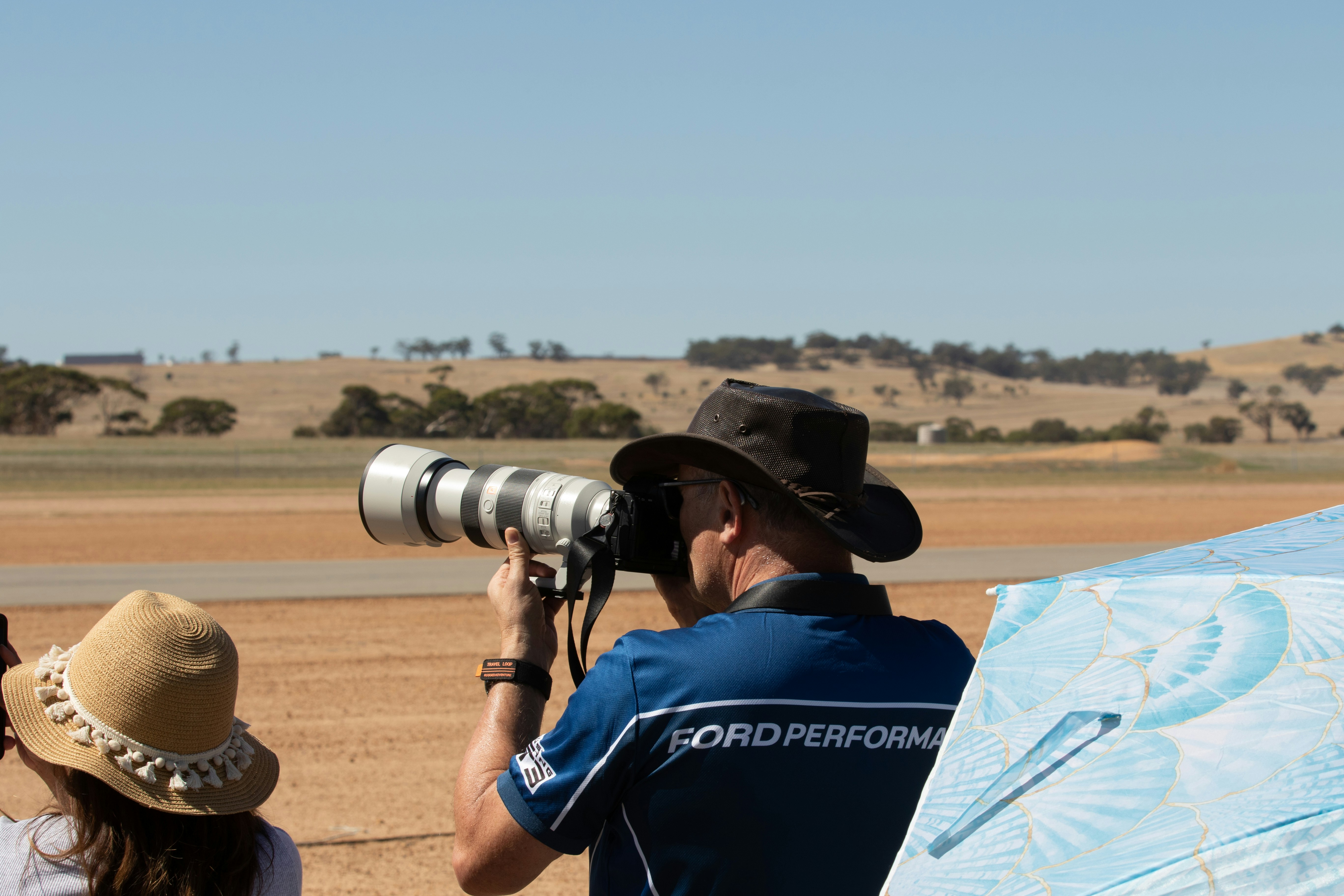 Fotógrafo carregando objetiva zoom pesada em sessão externa com postura de fadiga visível