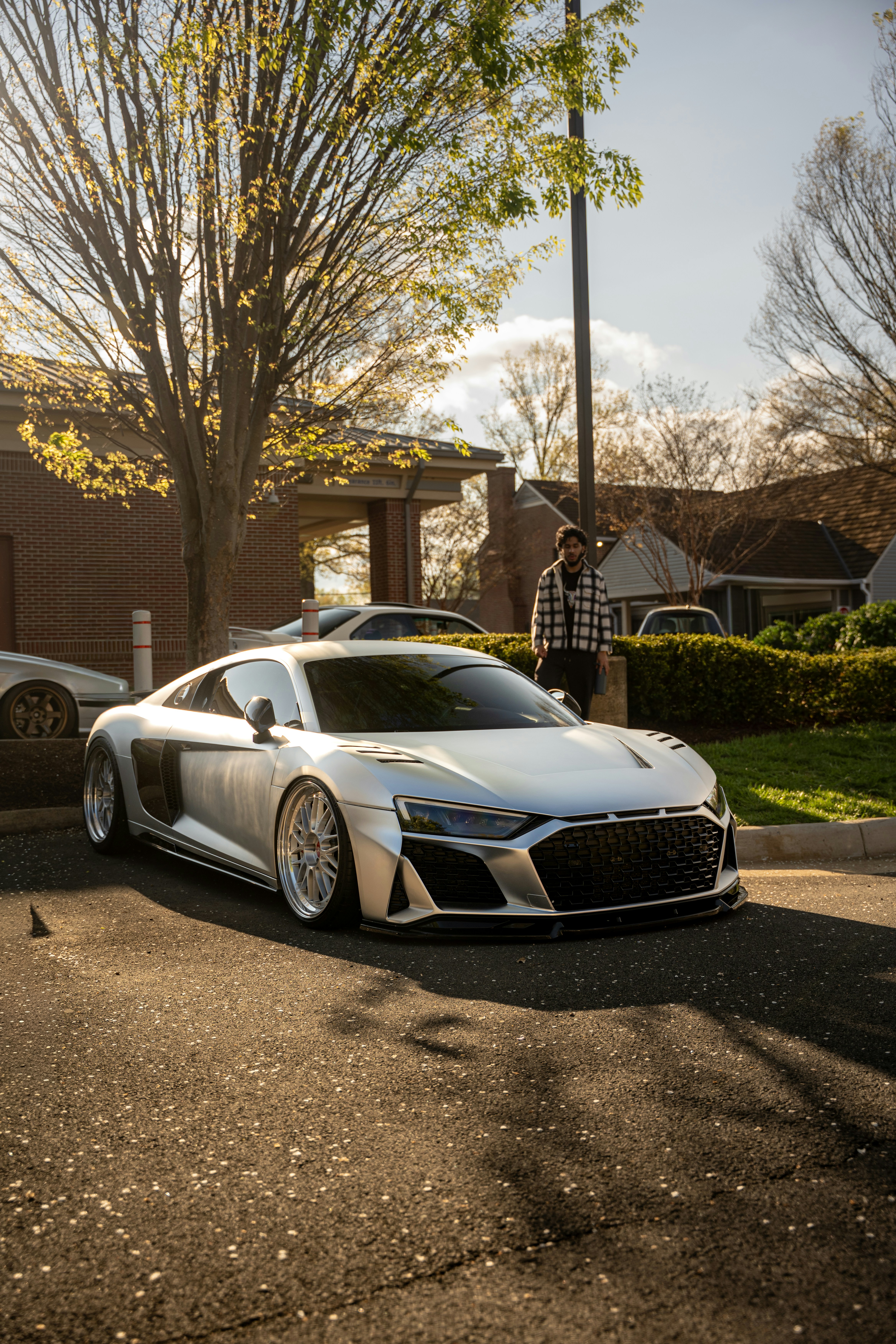 Silver sports car parked on asphalt with trees and building.