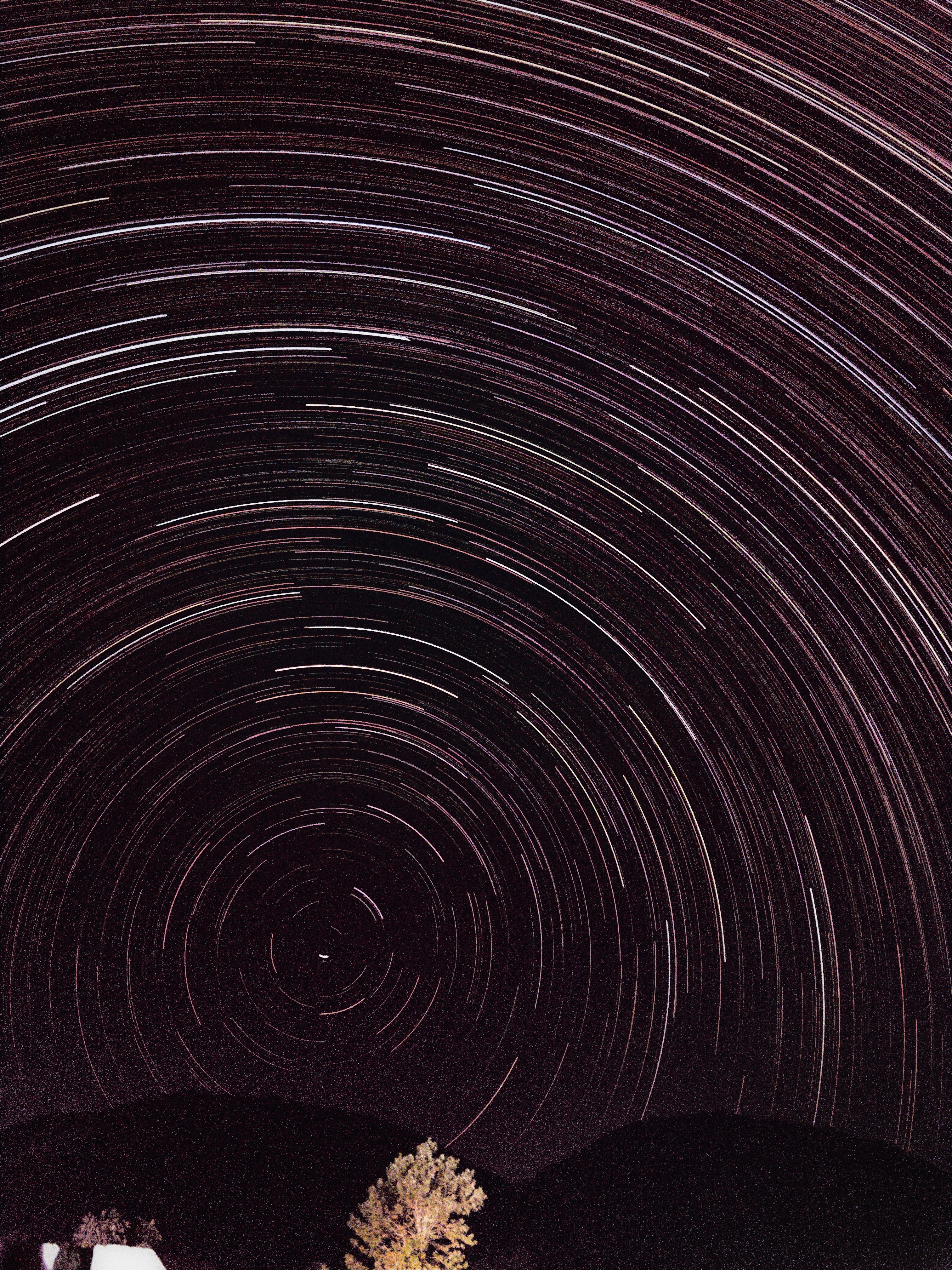 Star trails circle the night sky over dark hills