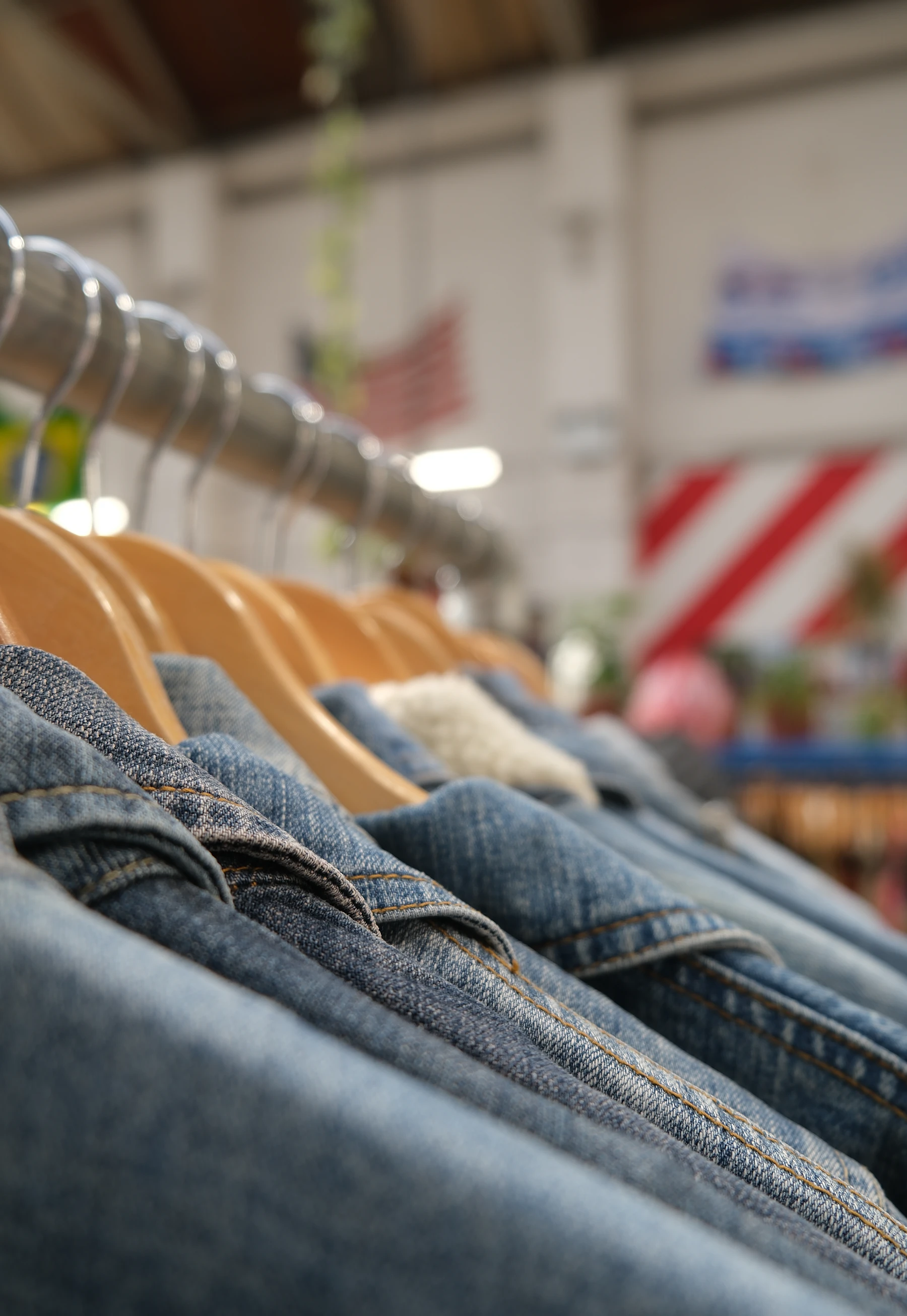 Denim jackets hanging shoulder to shoulder on wide wooden hangers along a steel rail