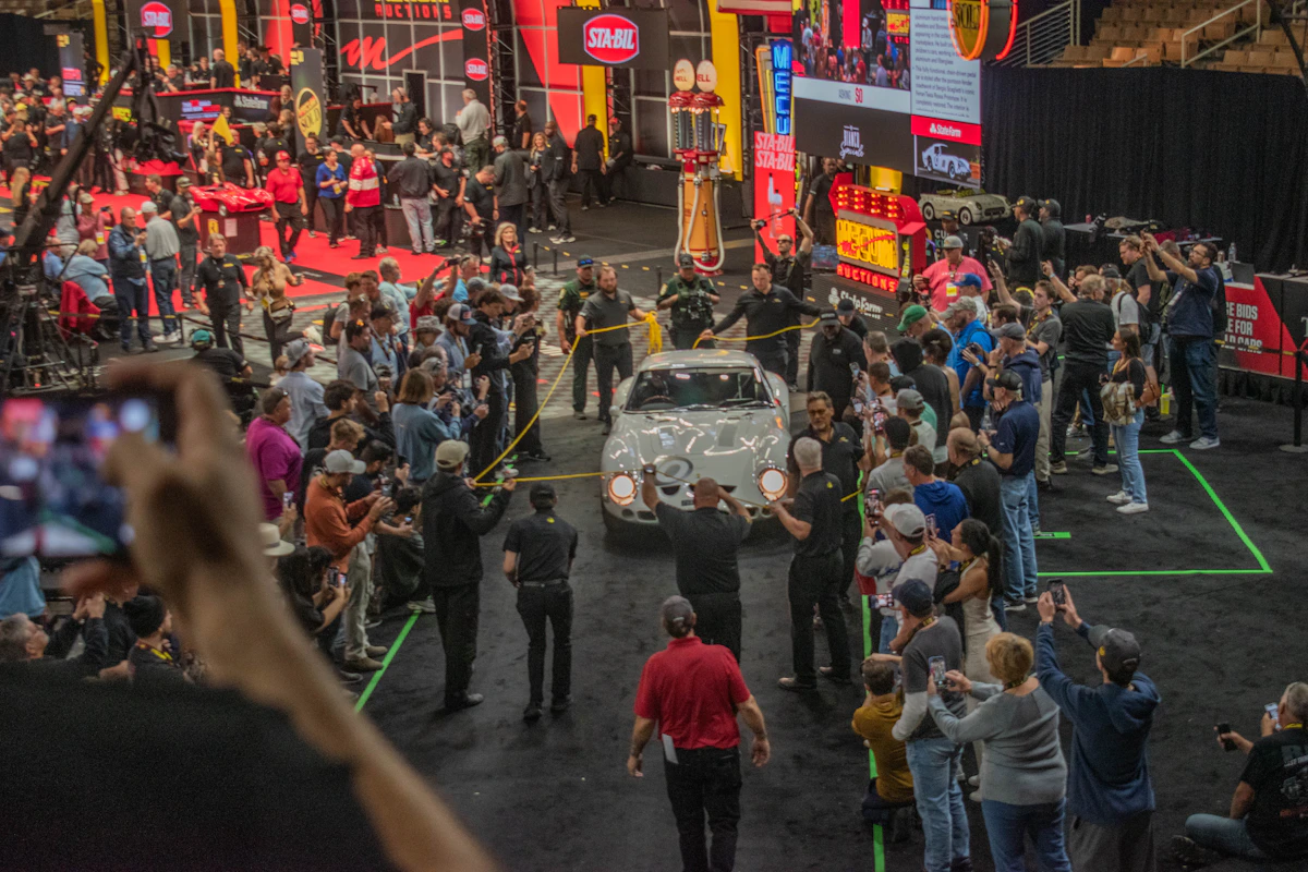 A crowd watching a car being presented at a live auction, analogous to how winning a bid and knowing the true value of what was won can be two separate things that only careful scoring can tell apart