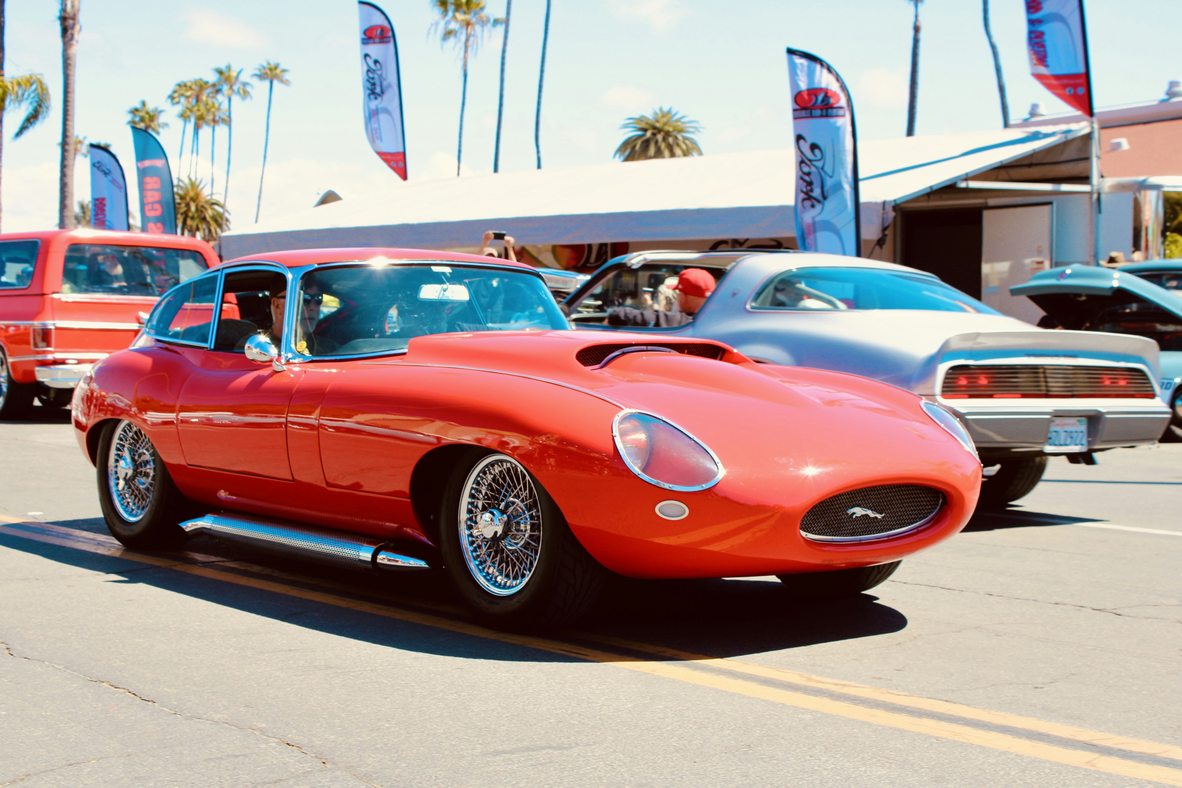 A bright red vintage car drives down a street.