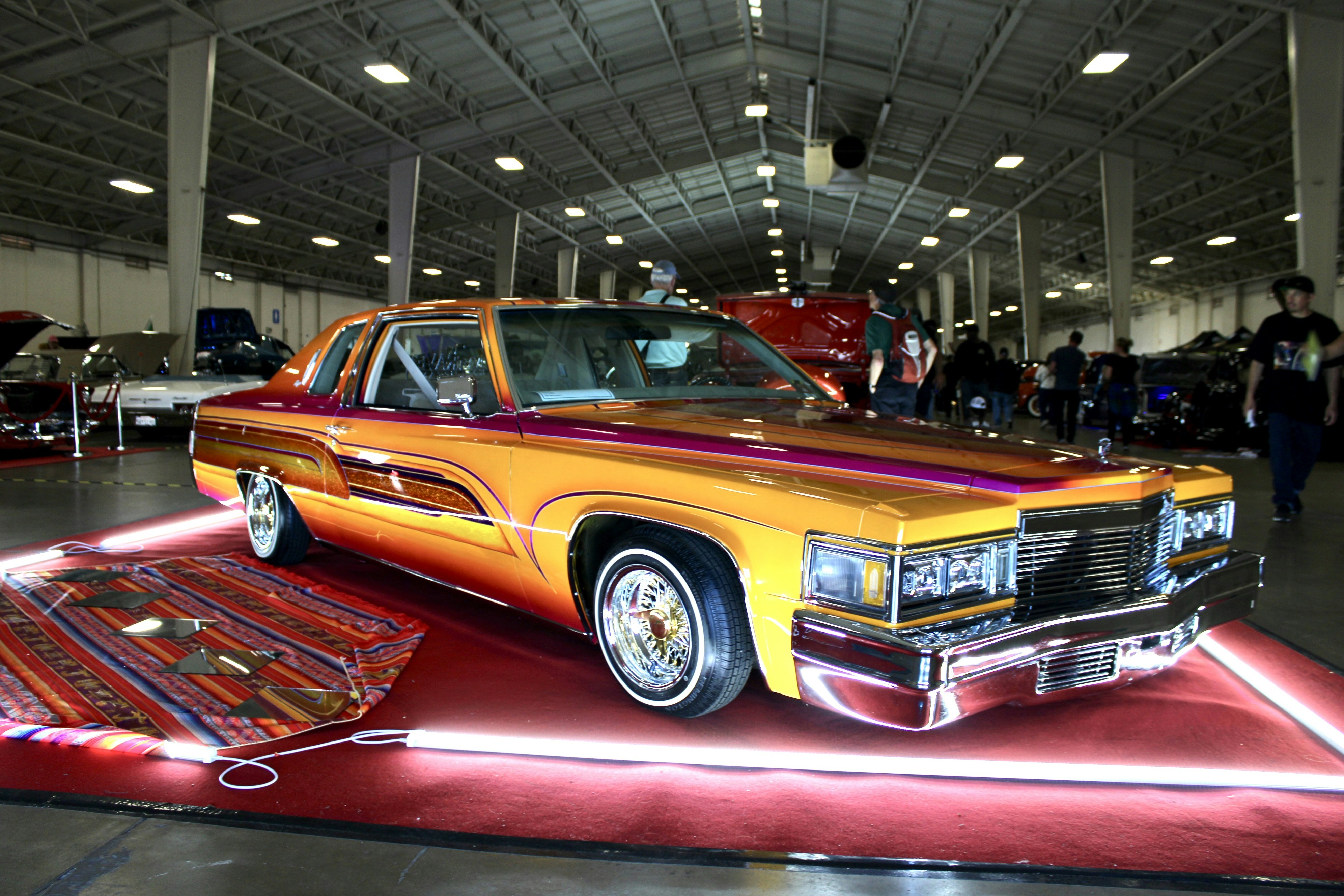 A classic lowrider cadillac with vibrant orange and yellow paint.