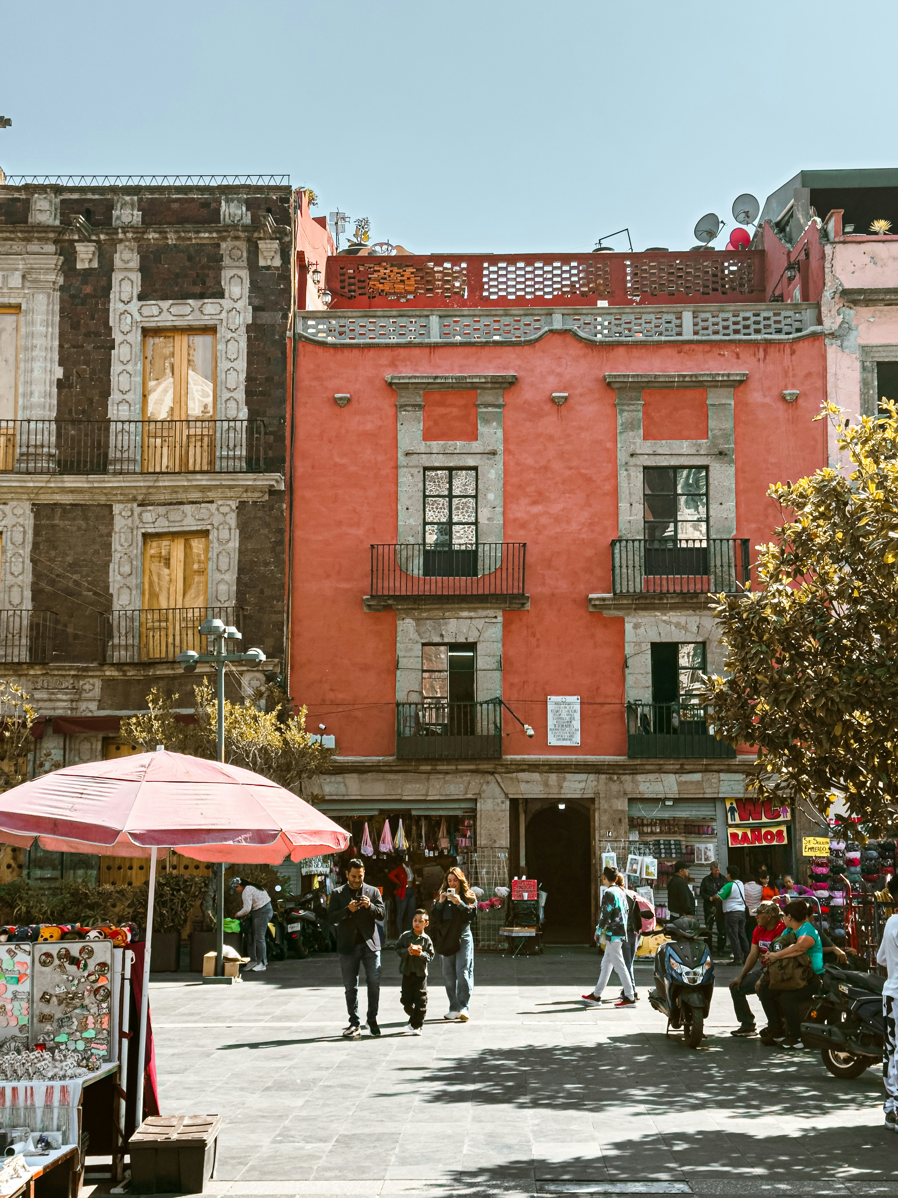 Persone che passano davanti a edifici colorati e bancarelle di mercato.