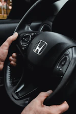 Hands gripping a honda steering wheel inside a car.