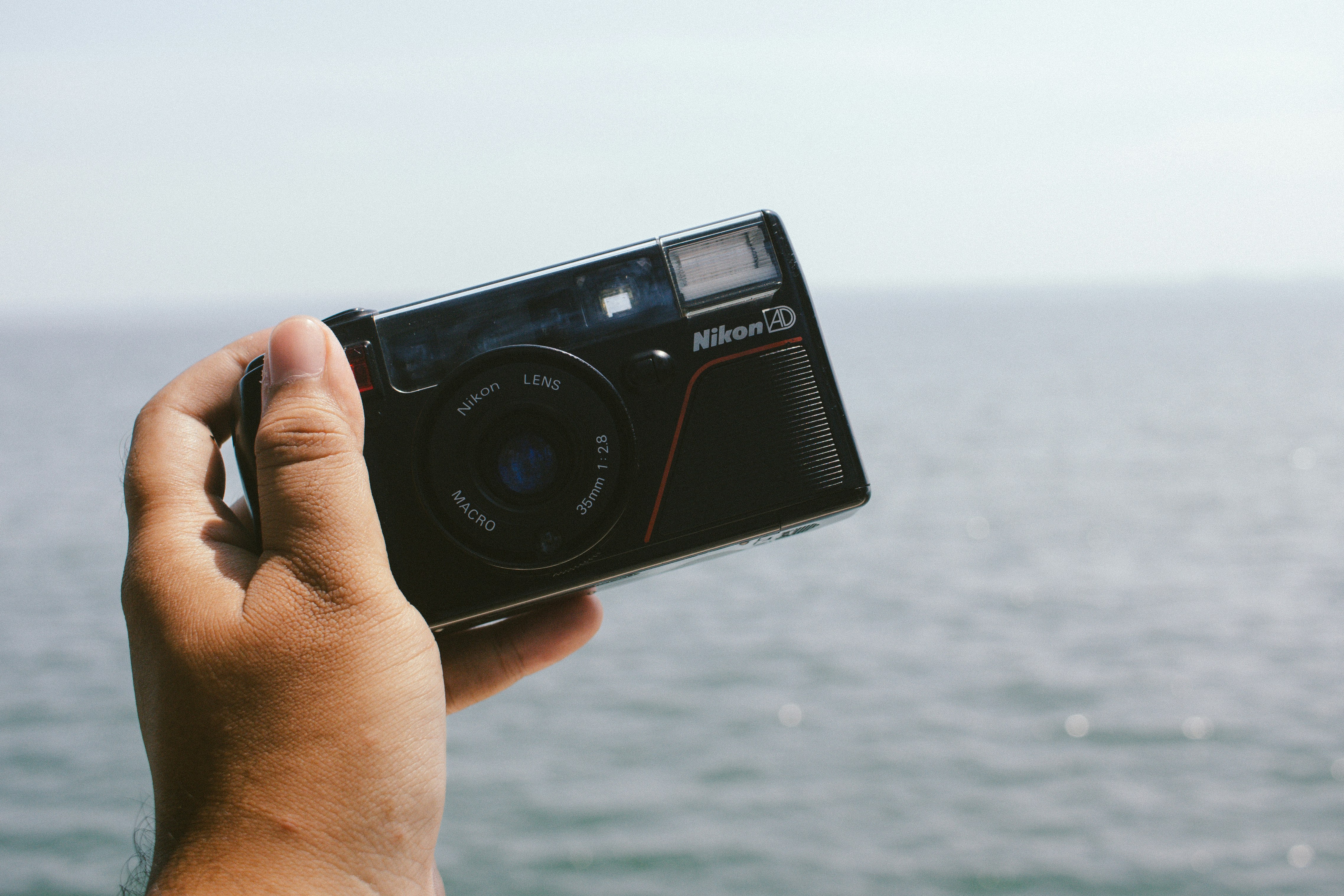 Hand holding a vintage nikon camera by the sea