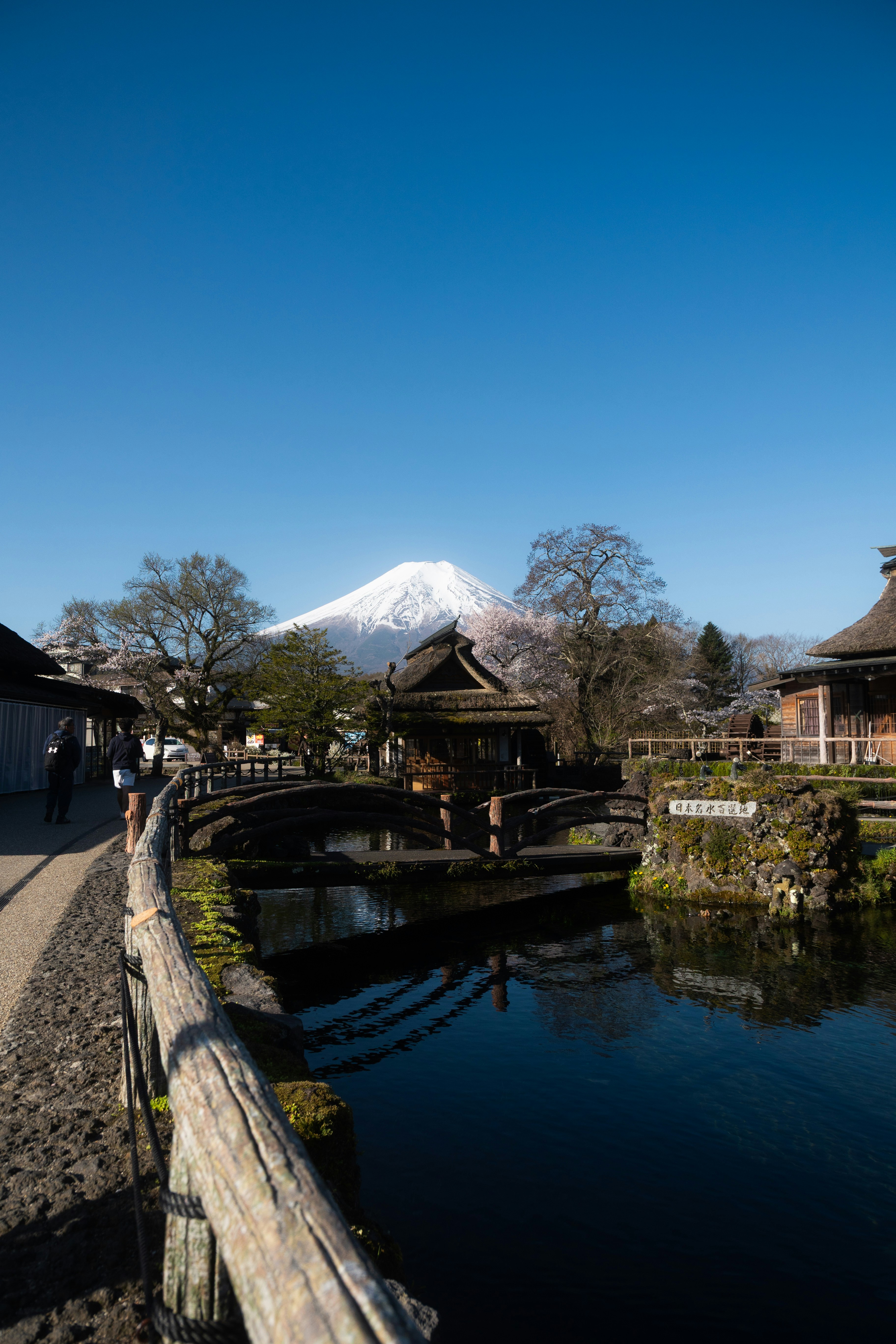 Snow-capped mount fuji overlooks a tranquil village with a canal.
