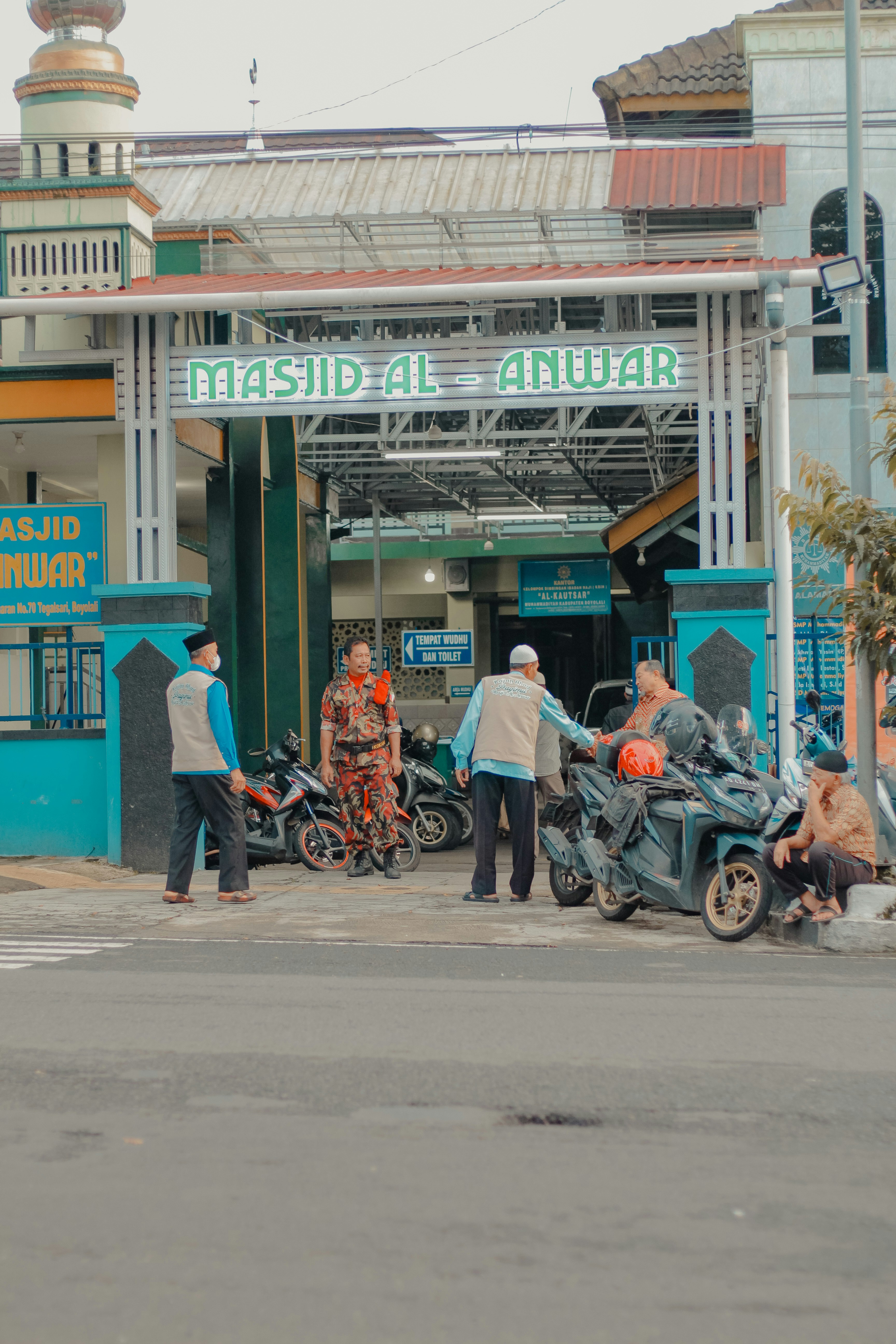 Orang-orang berkumpul di luar masjid al anwar dengan sepeda motor