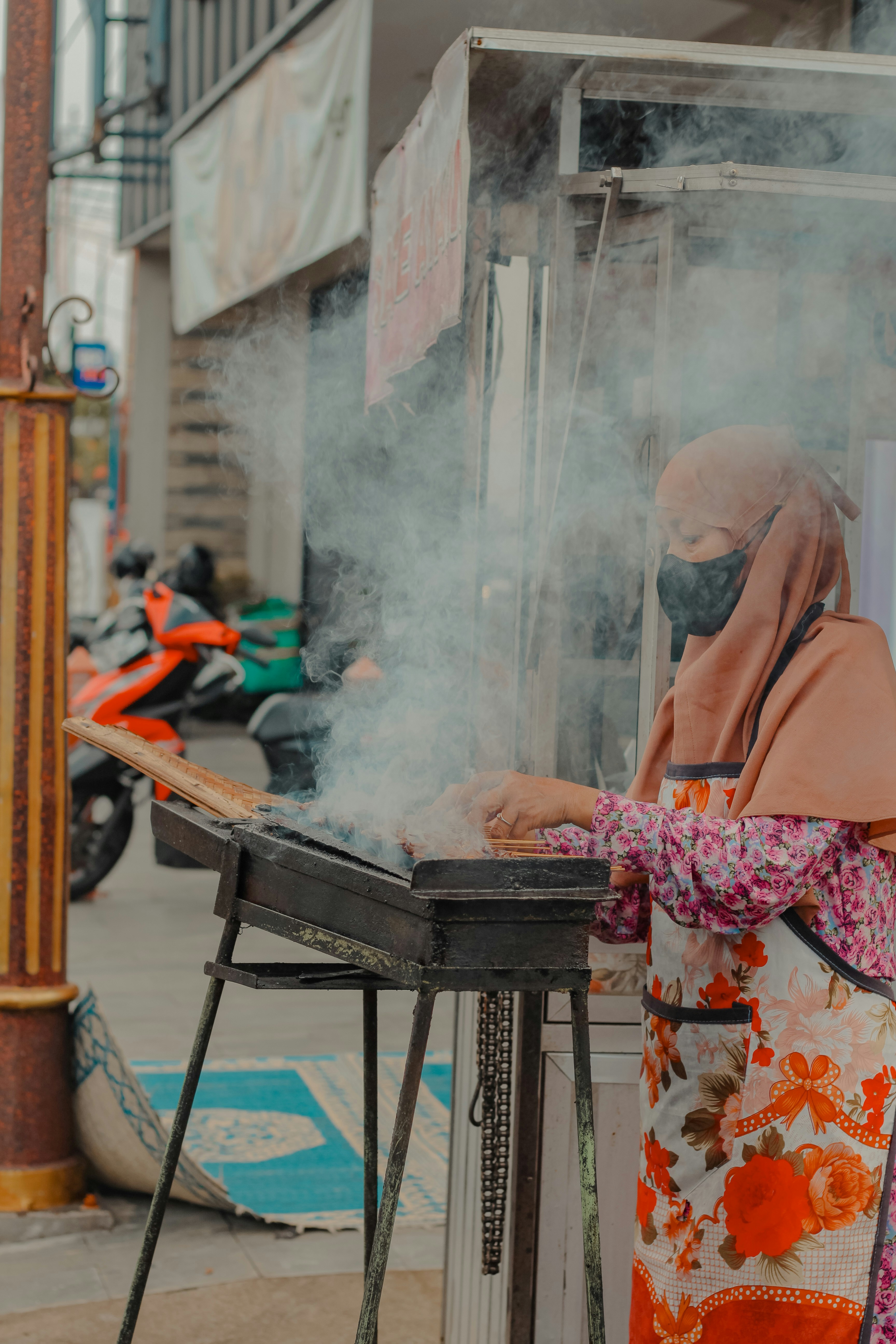 Woman in hijab and mask cooking outdoors
