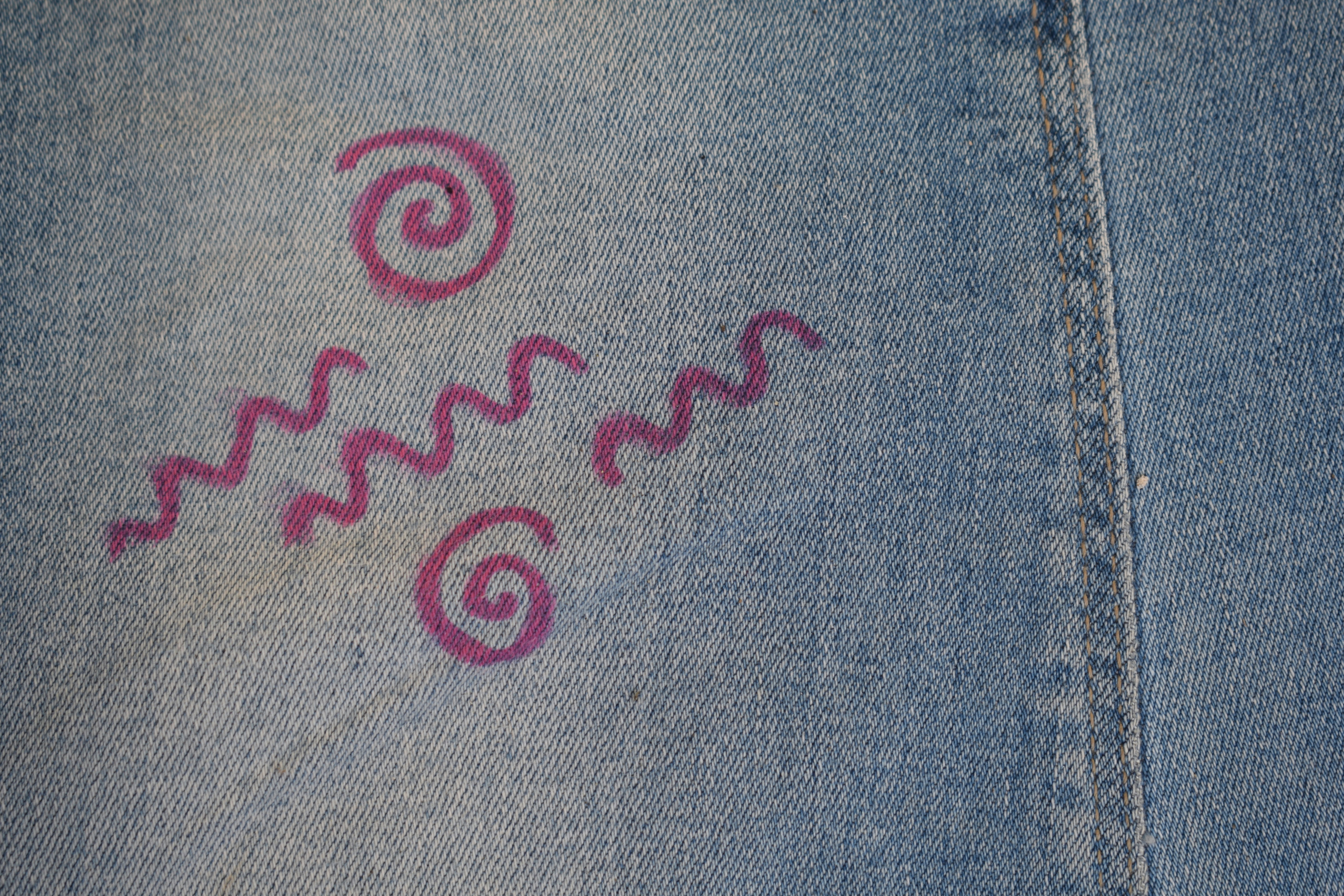 Purple swirls and waves drawn on denim fabric.