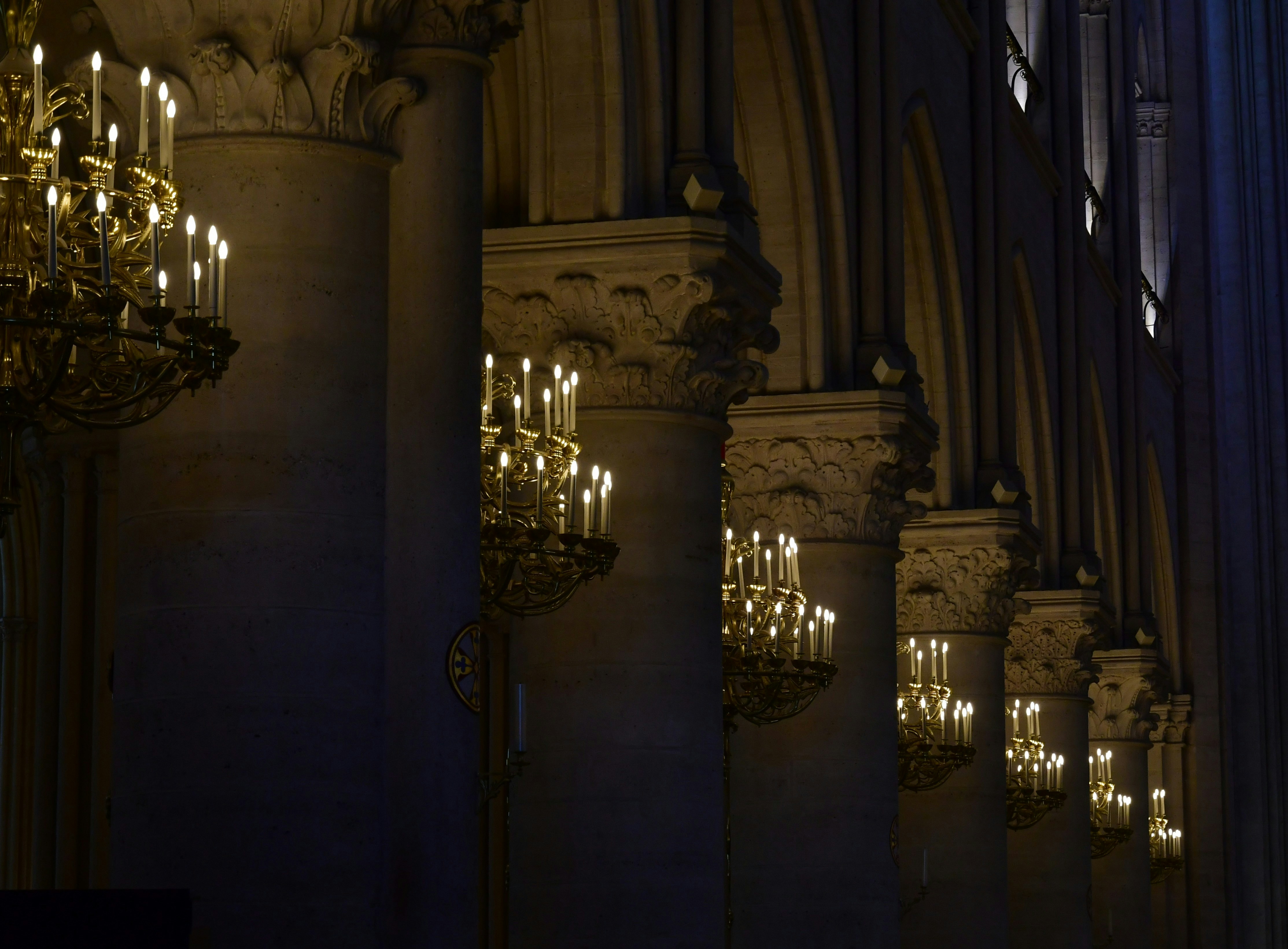 Ornate chandeliers illuminate a grand hall with stone columns.