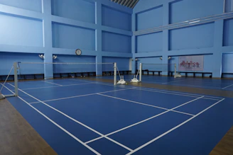 Empty indoor badminton courts with blue flooring.