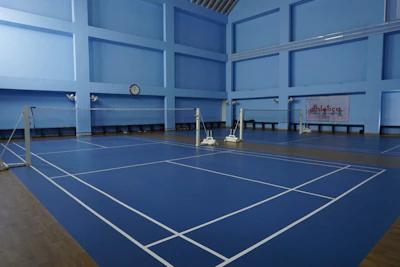 Empty indoor badminton courts with blue flooring.