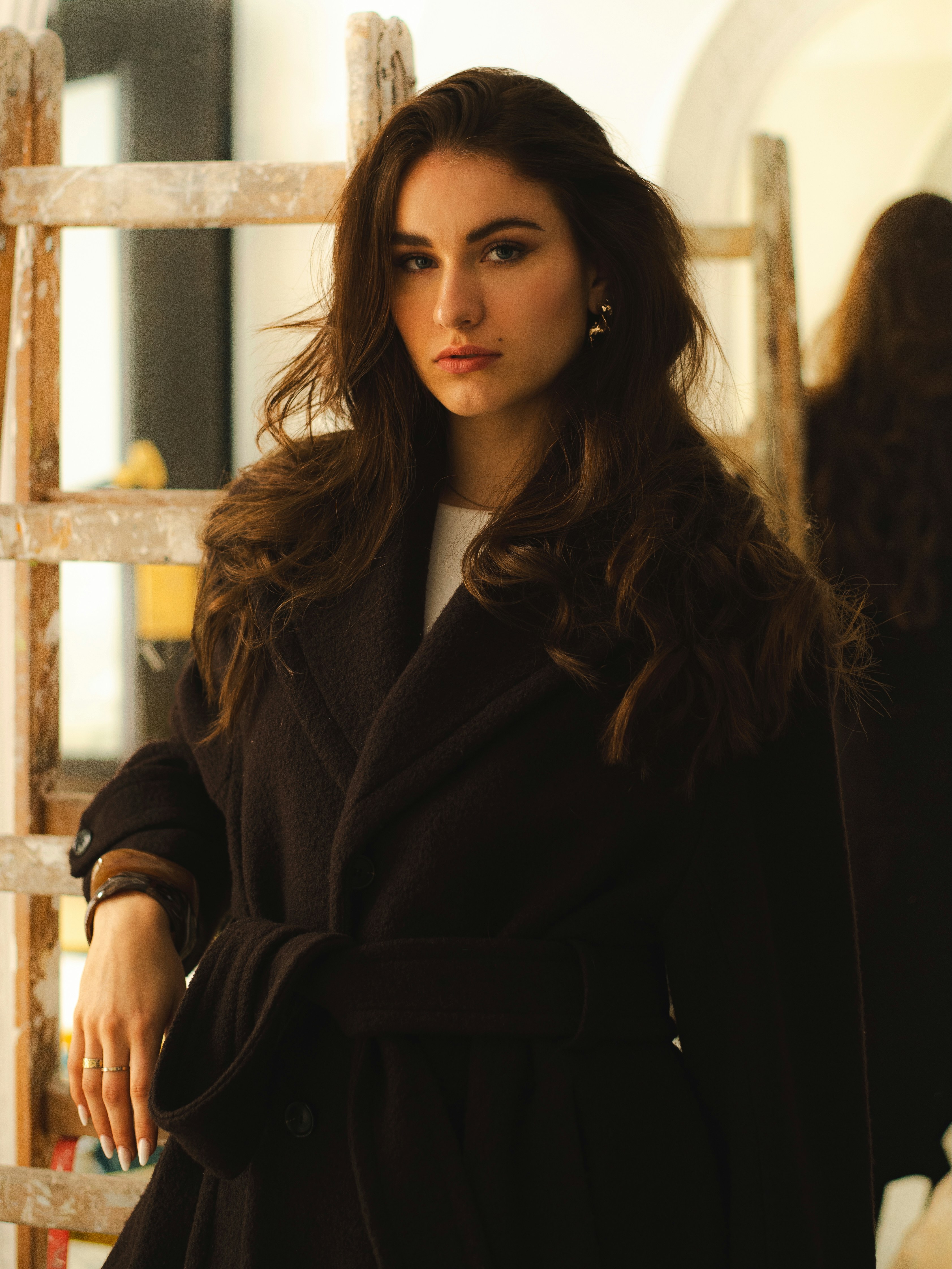 Eine Frau in einem schwarzen Mantel lehnt an einer Leiter.