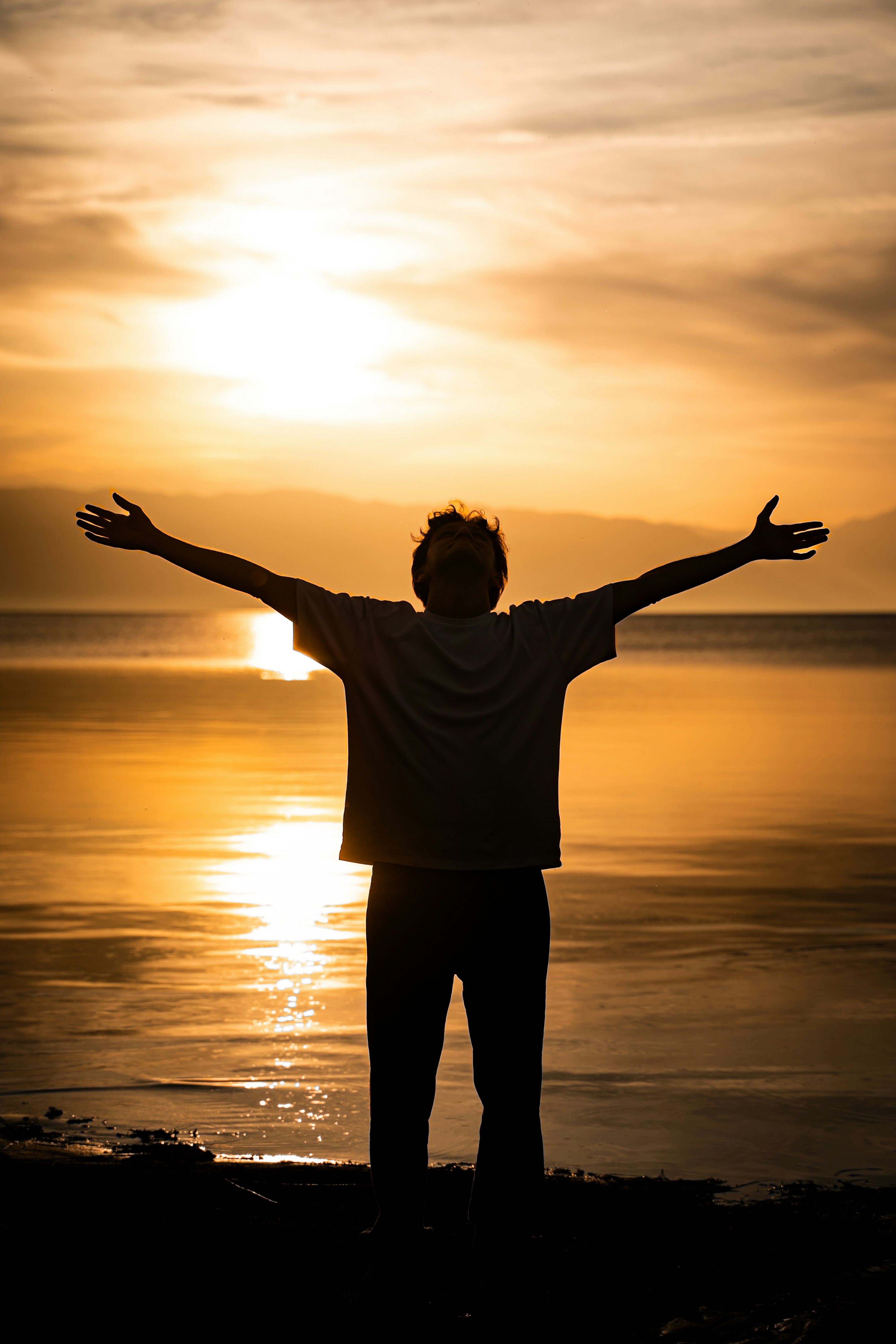 Person with arms outstretched facing sunset over water