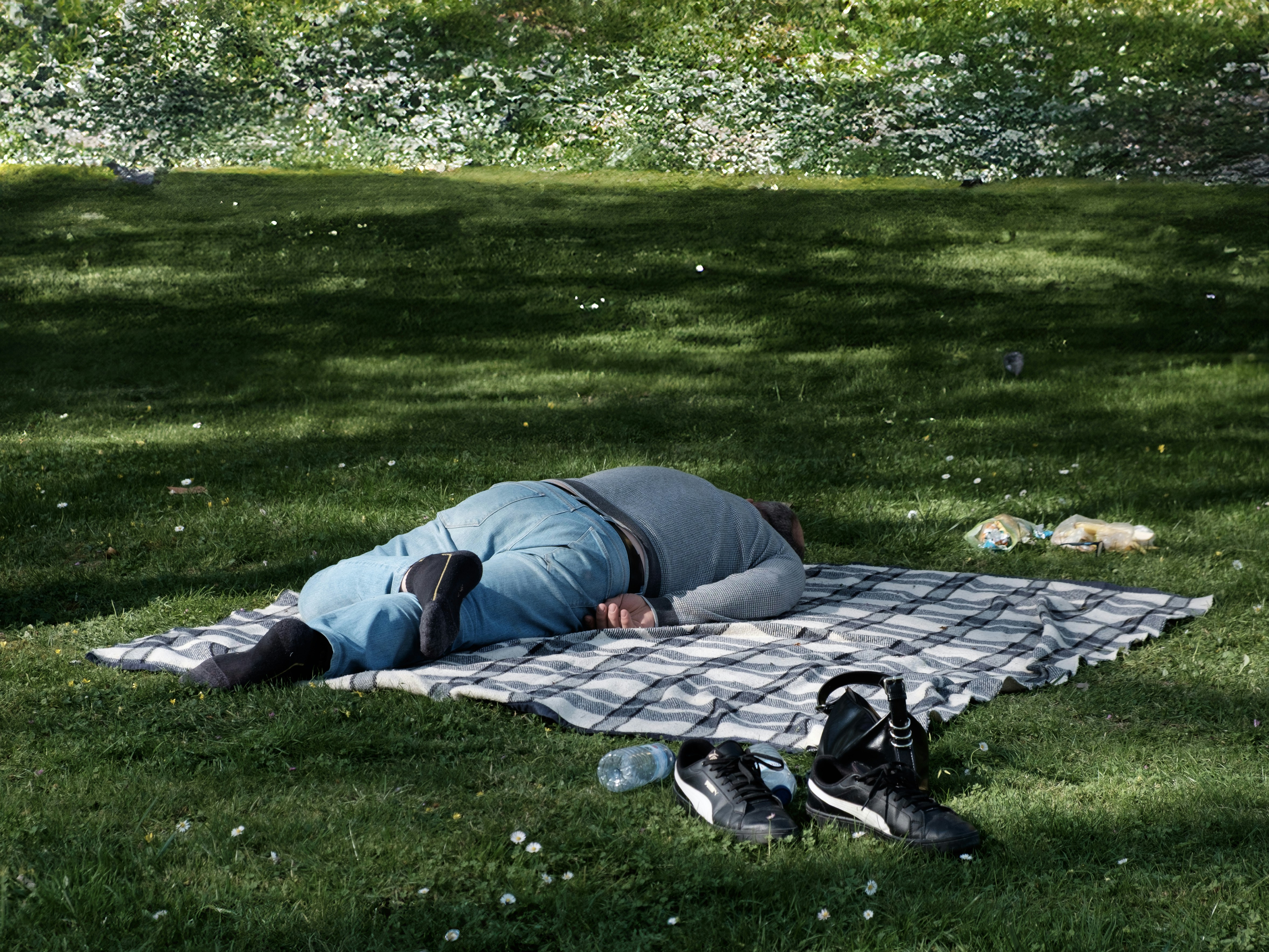 Man sleeping on a picnic blanket in a grassy park.
