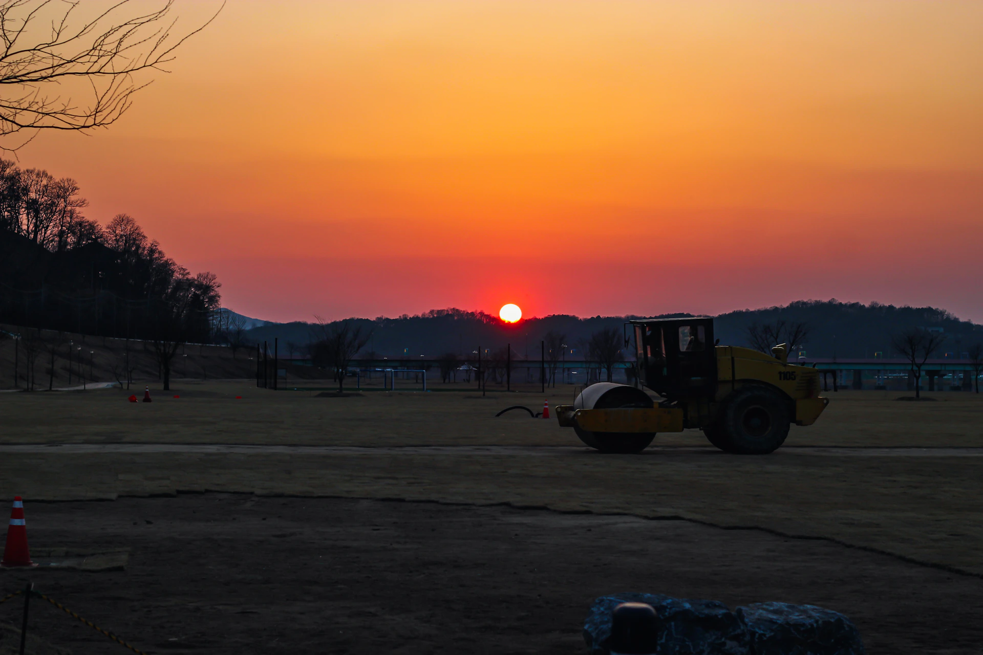 A steamroller on a field during a vibrant sunset.